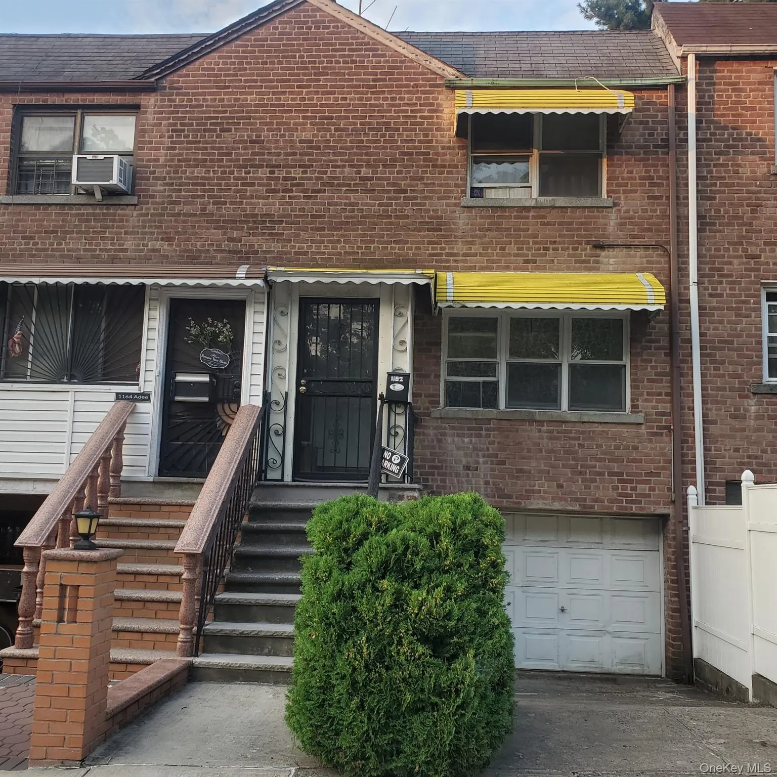 Brick facade featuring two entry doors with security gates, a ground-level garage, and yellow awnings over windows Brick facade featuring two entry doors with security gates, a ground-level garage, and yellow awnings over windows