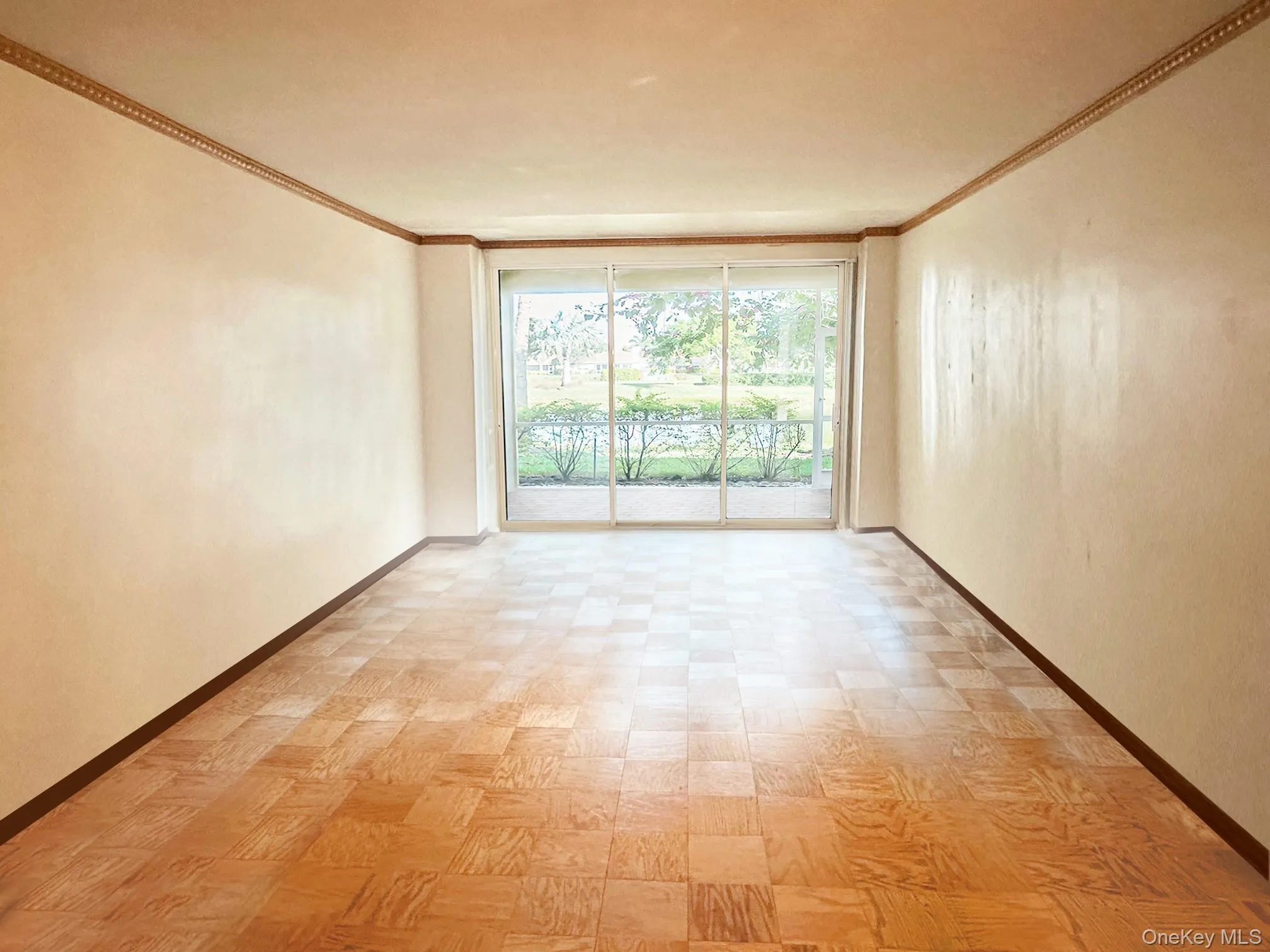 Expansive room featuring wood-finish flooring, decorative crown molding, and a full-width sliding glass door Expansive room featuring wood-finish flooring, decorative crown molding, and a full-width sliding glass door
