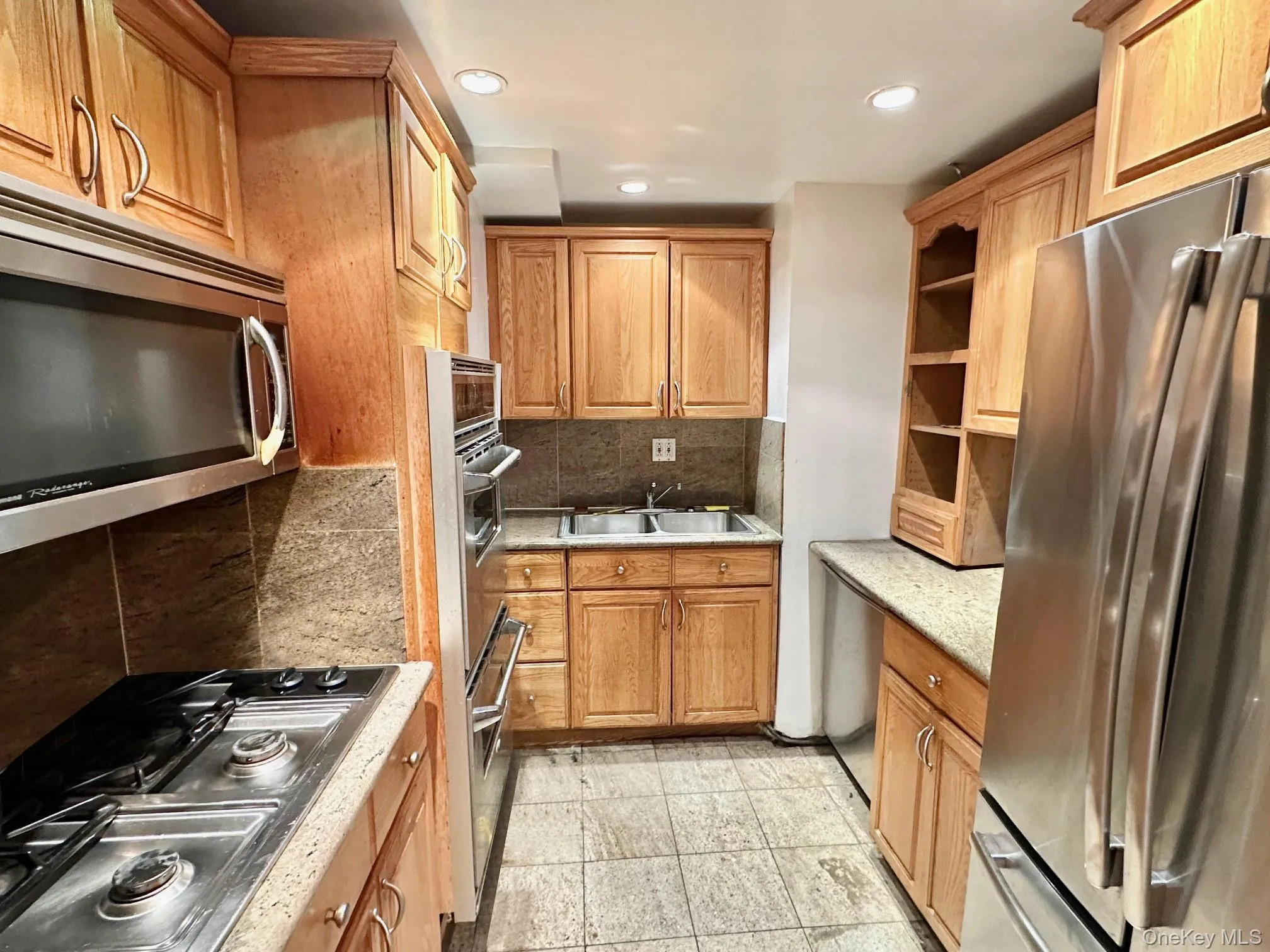 Kitchen featuring wood cabinetry, stainless steel appliances, stone countertops, a tile backsplash, and tile flooring Kitchen featuring wood cabinetry, stainless steel appliances, stone countertops, a tile backsplash, and tile flooring