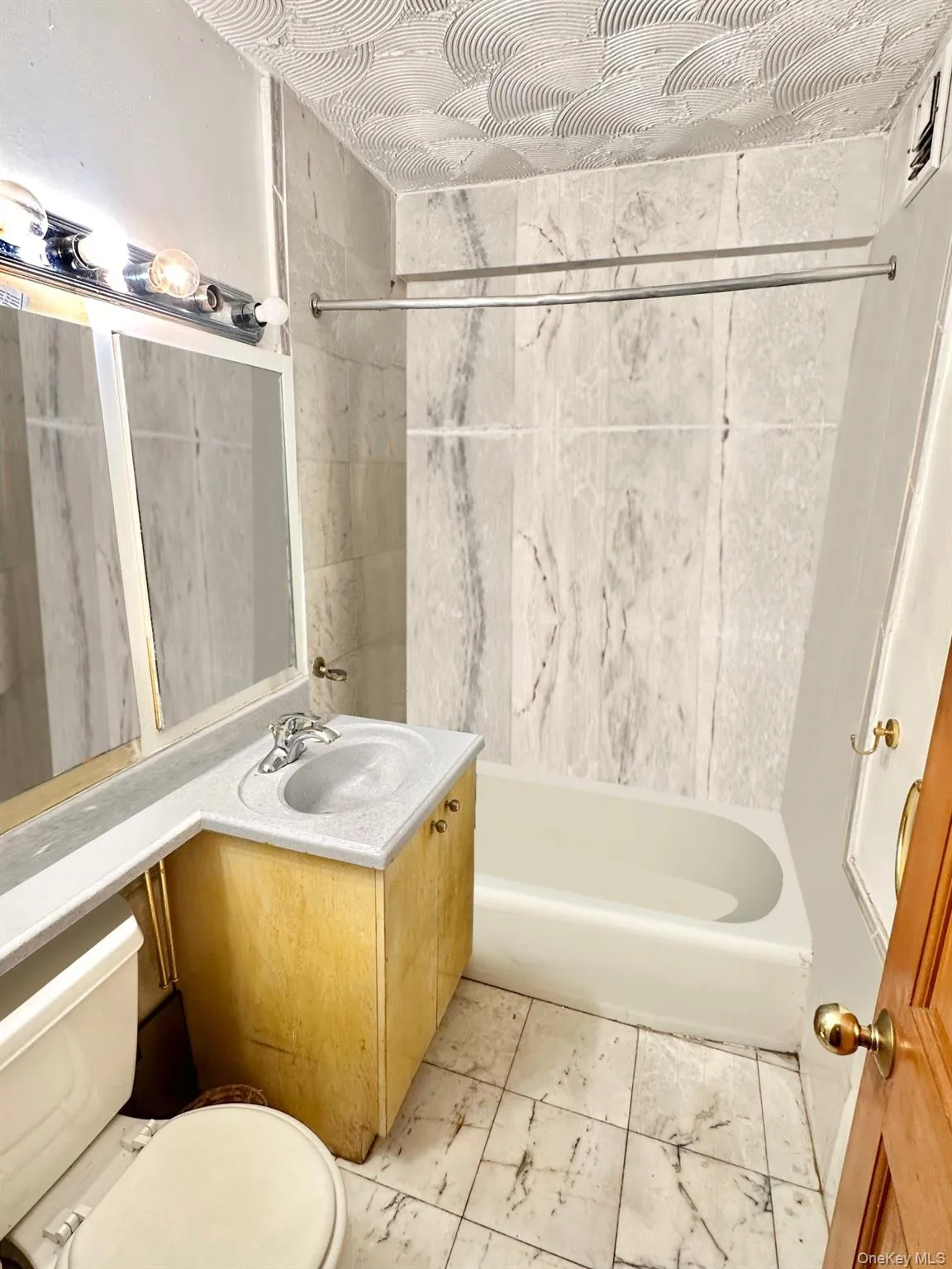 Bathroom featuring a white bathtub, marbled tile shower surround, and a single vanity with storage cabinetry Bathroom featuring a white bathtub, marbled tile shower surround, and a single vanity with storage cabinetry
