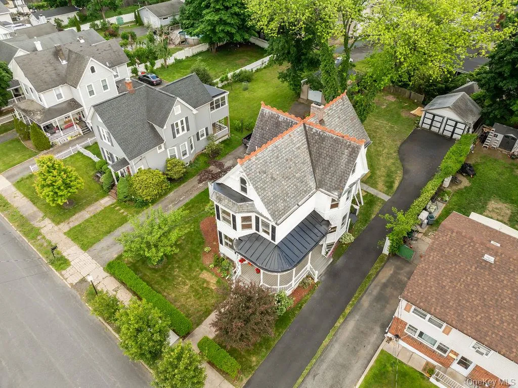 Victorian-style residence featuring white siding, a multi-gabled roofline with slate shingles, and a curved porch with a black standing seam roof Victorian-style residence featuring white siding, a multi-gabled roofline with slate shingles, and a curved porch with a black standing seam roof