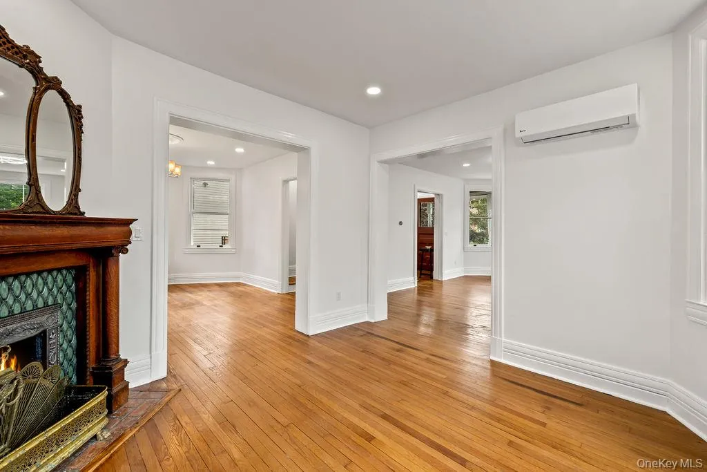 Hardwood flooring throughout, featuring a decorative fireplace with a detailed wooden mantel and green tile surround Hardwood flooring throughout, featuring a decorative fireplace with a detailed wooden mantel and green tile surround