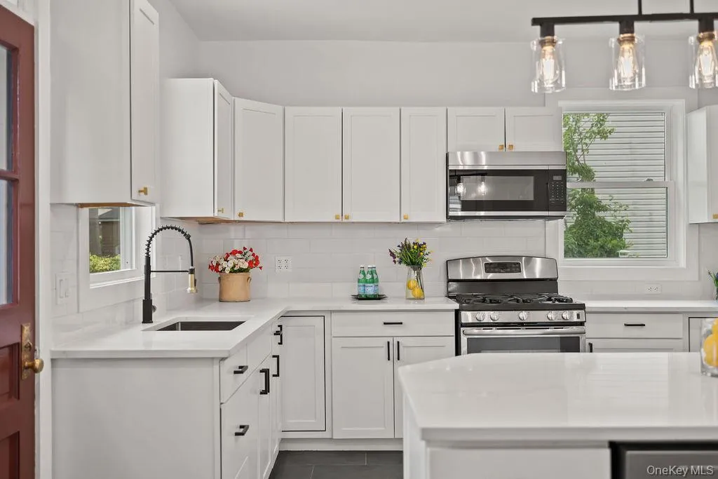 White cabinetry with gold-tone hardware, stainless steel appliances, white subway tile backsplash, and dark grey tile flooring White cabinetry with gold-tone hardware, stainless steel appliances, white subway tile backsplash, and dark grey tile flooring