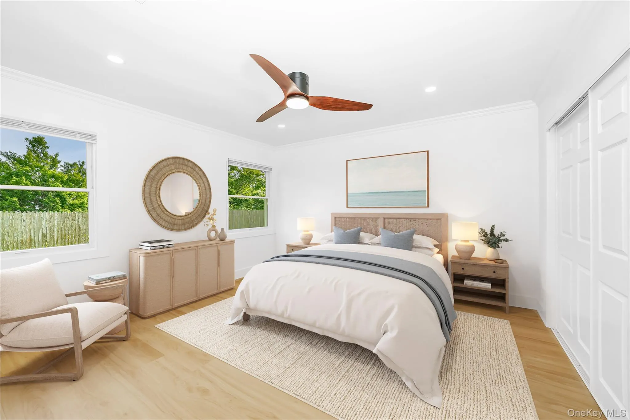 Bright interior featuring wood-finish flooring, two large windows, a ceiling fan with light, crown molding, and sliding panel closet doors Bright interior featuring wood-finish flooring, two large windows, a ceiling fan with light, crown molding, and sliding panel closet doors