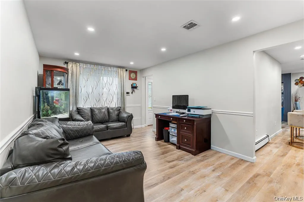 Spacious living area featuring wood-finish flooring, recessed lighting, and a white interior door with decorative glass panels Spacious living area featuring wood-finish flooring, recessed lighting, and a white interior door with decorative glass panels