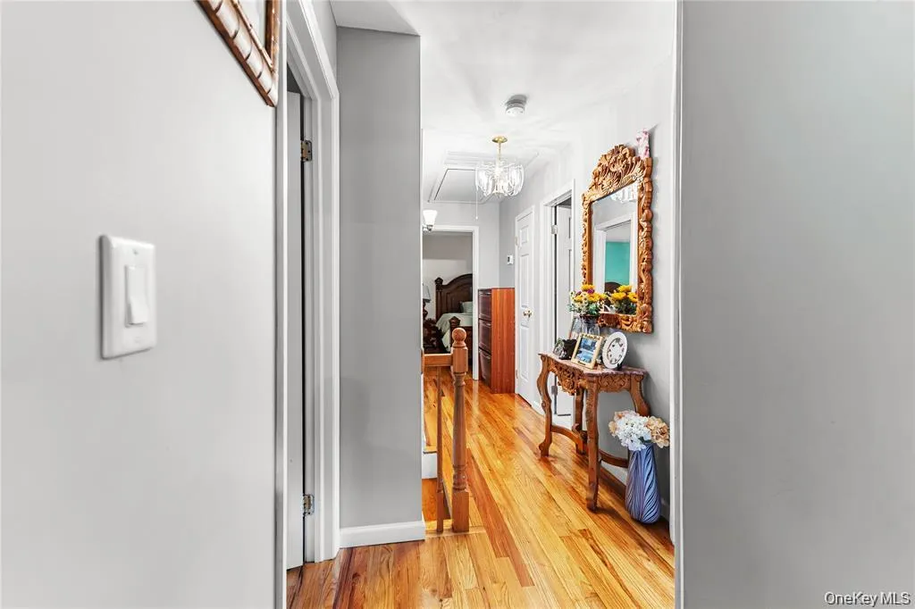 Hallway featuring wood-finish flooring, light grey walls, white trim, and a decorative overhead light fixture Hallway featuring wood-finish flooring, light grey walls, white trim, and a decorative overhead light fixture