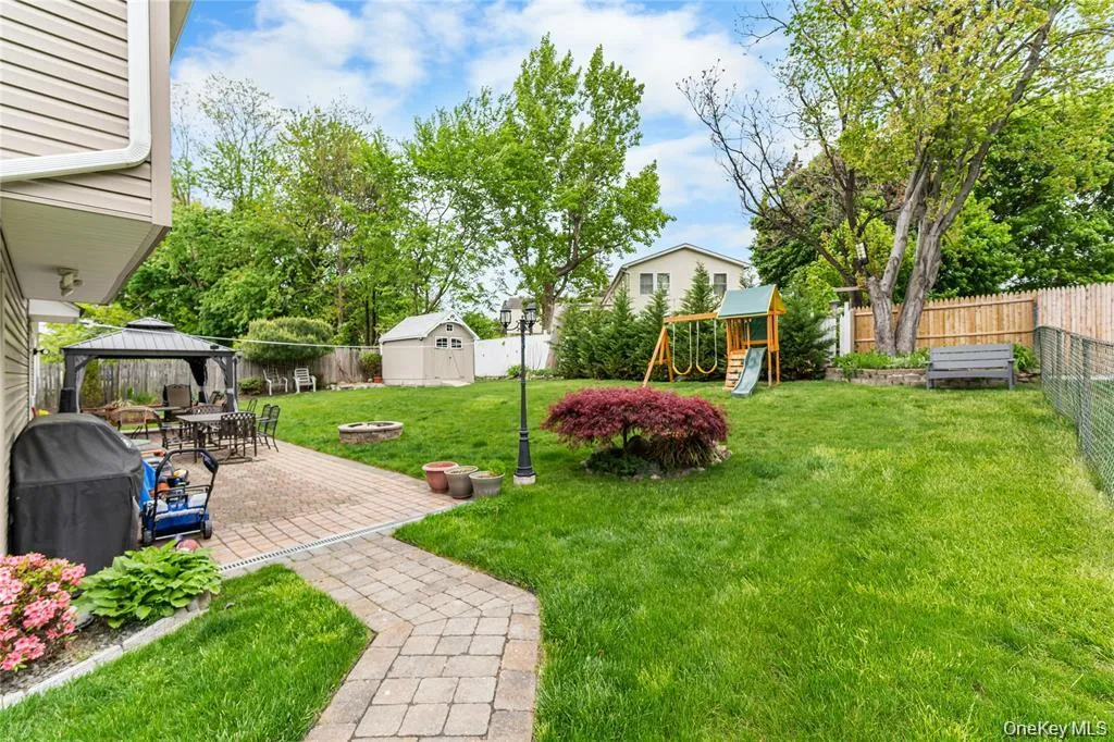 Expansive backyard featuring a paved patio area, a separate paved pathway, a storage shed, a wooden fence, and mature landscaping Expansive backyard featuring a paved patio area, a separate paved pathway, a storage shed, a wooden fence, and mature landscaping
