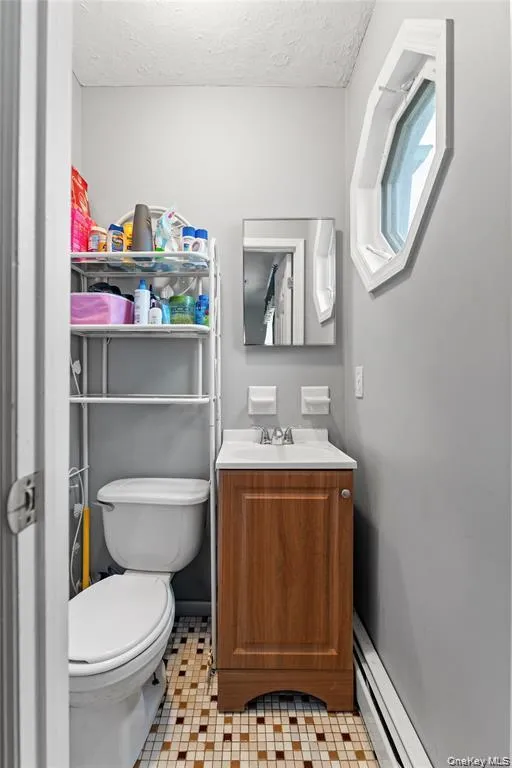 Powder room featuring a unique octagonal window, a wood-finish vanity with an integrated sink, a commode, and mosaic tile flooring Powder room featuring a unique octagonal window, a wood-finish vanity with an integrated sink, a commode, and mosaic tile flooring
