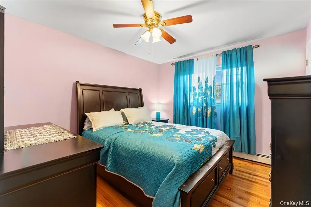 Bedroom featuring hardwood flooring, a ceiling fan with light fixture, and a window with curtains Bedroom featuring hardwood flooring, a ceiling fan with light fixture, and a window with curtains