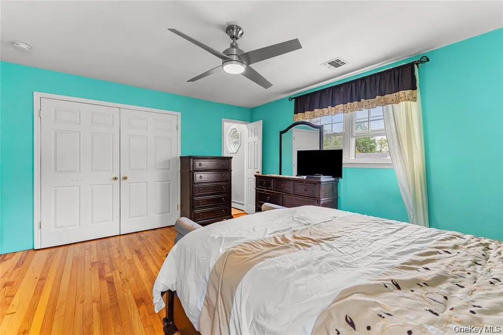 Bedroom featuring wood-finish flooring, a ceiling fan with integrated lighting, and a double-panel closet with brass hardware Bedroom featuring wood-finish flooring, a ceiling fan with integrated lighting, and a double-panel closet with brass hardware