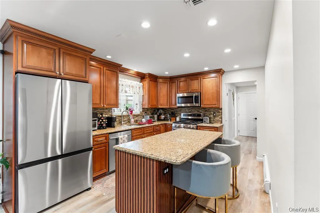 Kitchen featuring wood cabinetry with crown molding, stainless steel appliances, recessed lighting, and a granite island with built-in seating Kitchen featuring wood cabinetry with crown molding, stainless steel appliances, recessed lighting, and a granite island with built-in seating