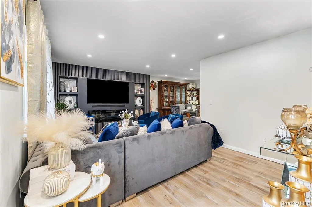 Open-concept living area featuring wood-finish flooring, recessed lighting, and a prominent built-in media wall with shelving Open-concept living area featuring wood-finish flooring, recessed lighting, and a prominent built-in media wall with shelving