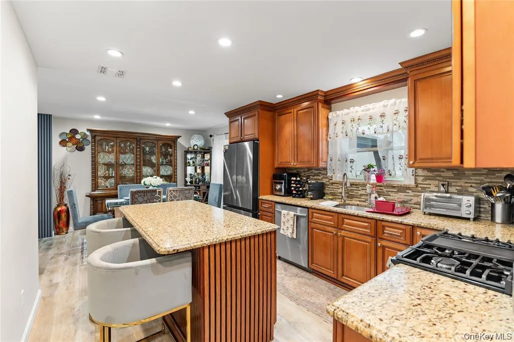 Open-concept kitchen featuring light-toned wood cabinetry, granite countertops, a built-in gas range, and a mosaic tile backsplash Open-concept kitchen featuring light-toned wood cabinetry, granite countertops, a built-in gas range, and a mosaic tile backsplash