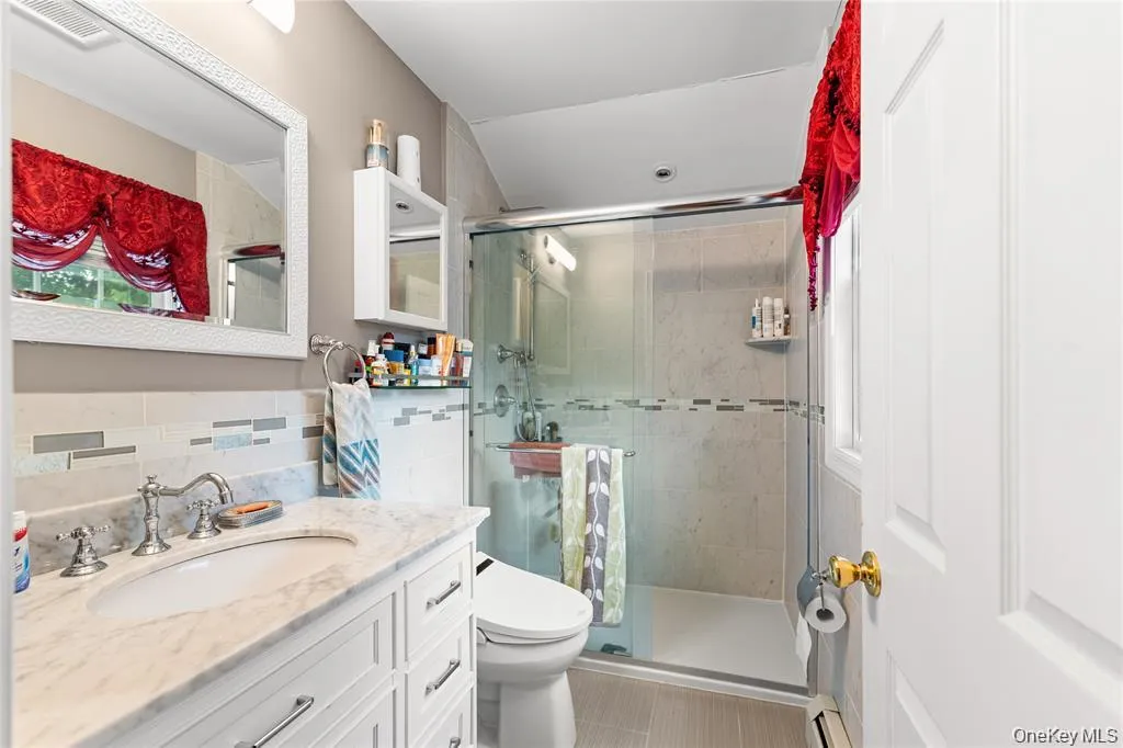 Bathroom featuring a frameless glass shower enclosure, white vanity with a marble-finish countertop, undermount sink, and polished chrome fixtures Bathroom featuring a frameless glass shower enclosure, white vanity with a marble-finish countertop, undermount sink, and polished chrome fixtures