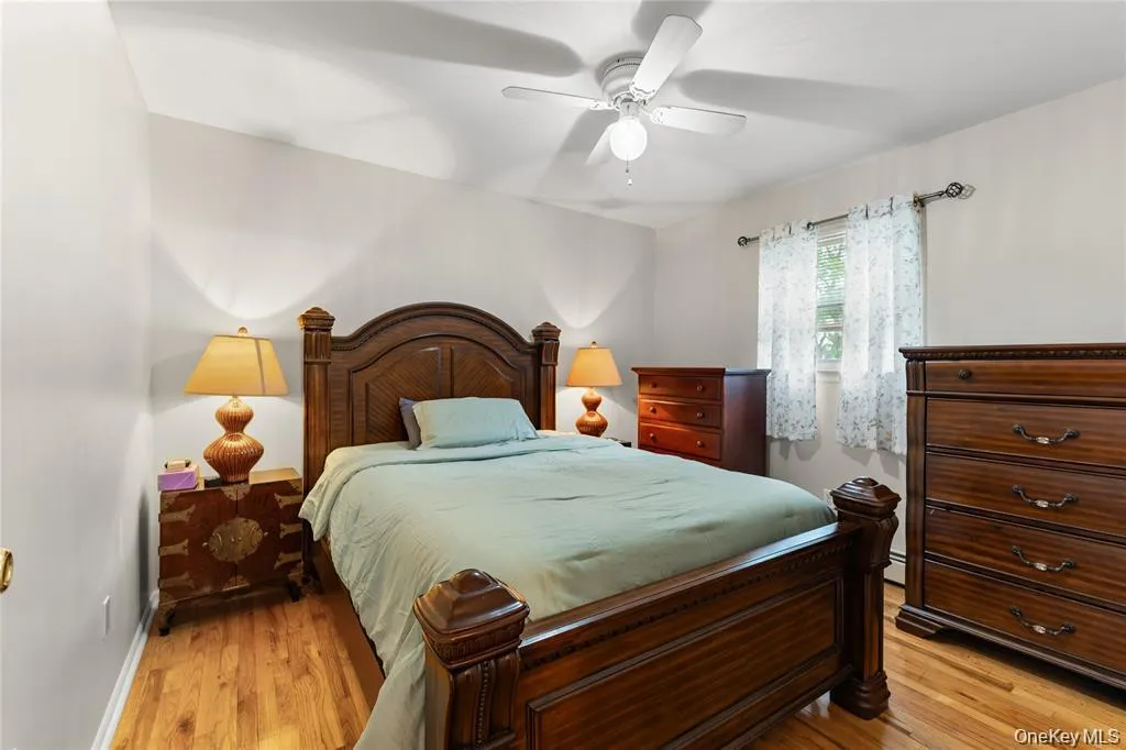 Bedroom featuring wood-finish flooring, a ceiling fan with integrated lighting, and a single window with decorative curtain rods Bedroom featuring wood-finish flooring, a ceiling fan with integrated lighting, and a single window with decorative curtain rods