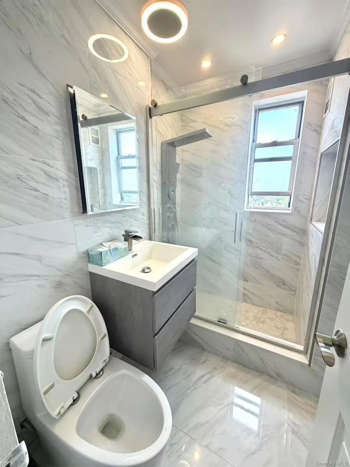 Bathroom featuring a floating vanity with a vessel sink, a glass-enclosed shower with a multi-function shower panel, and marble-look wall and floor tiling Bathroom featuring a floating vanity with a vessel sink, a glass-enclosed shower with a multi-function shower panel, and marble-look wall and floor tiling