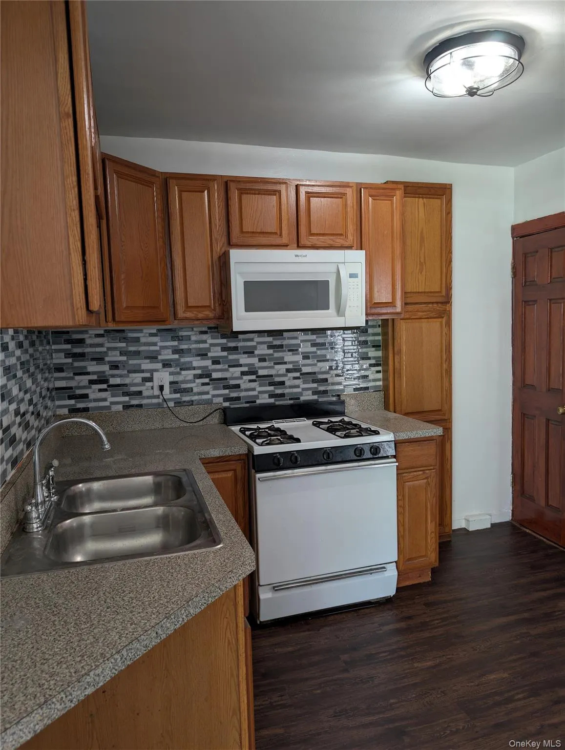 Kitchen featuring wood cabinetry, a mosaic tile backsplash, a double basin stainless steel sink, range and microwave. Kitchen featuring wood cabinetry, a mosaic tile backsplash, a double basin stainless steel sink, range and microwave.