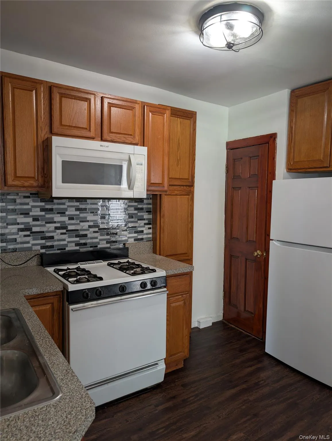 Kitchen featuring wood-finish flooring, wood cabinetry, stone-look countertops, and a mosaic tile backsplash Kitchen featuring wood-finish flooring, wood cabinetry, stone-look countertops, and a mosaic tile backsplash