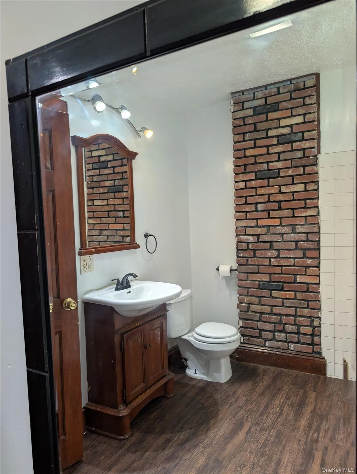 Vinyl wood-finish flooring with a white toilet, freestanding vanity, and a prominent brick accent wall Vinyl wood-finish flooring with a white toilet, freestanding vanity, and a prominent brick accent wall