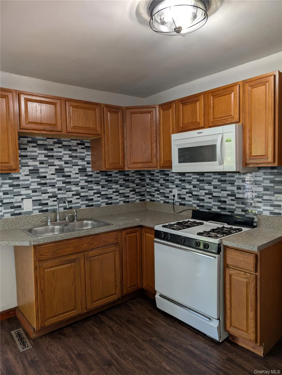 Updated kitchen featuring warm wood cabinetry, granite countertops, white appliances including a gas range and microwave, geometric tile backsplash Updated kitchen featuring warm wood cabinetry, granite countertops, white appliances including a gas range and microwave, geometric tile backsplash