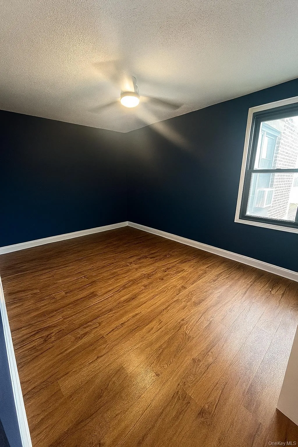 Empty room with wood finished floors, a textured ceiling, and a ceiling fan Empty room with wood finished floors, a textured ceiling, and a ceiling fan