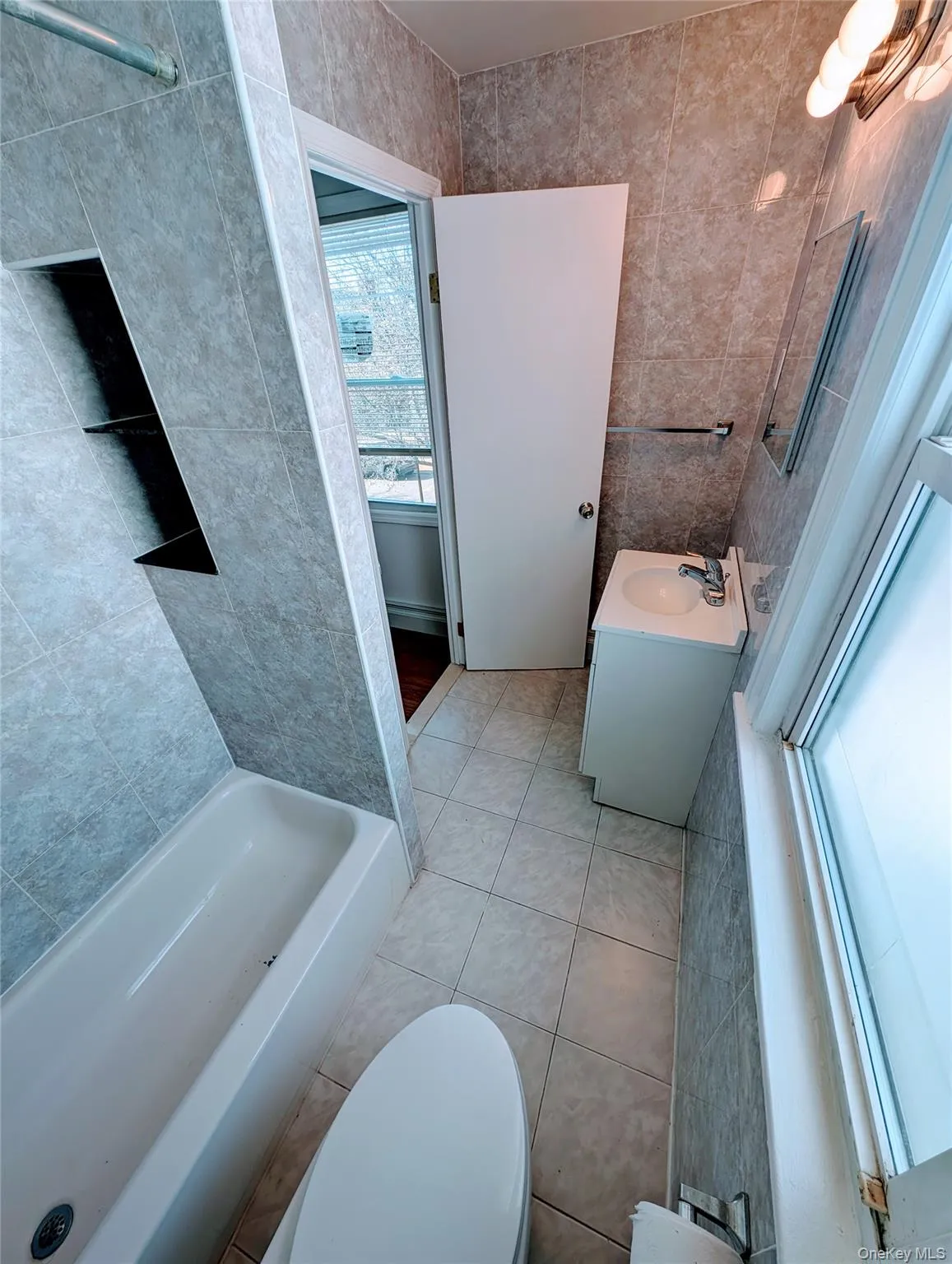 Bathroom featuring vanity, tile patterned floors, toilet, a tub to relax in, and tile walls Bathroom featuring vanity, tile patterned floors, toilet, a tub to relax in, and tile walls