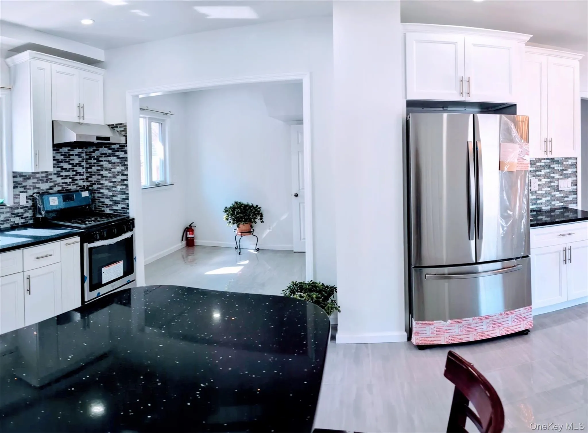 Kitchen with tasteful backsplash, under cabinet range hood, white cabinetry, and stainless steel appliances Kitchen with tasteful backsplash, under cabinet range hood, white cabinetry, and stainless steel appliances