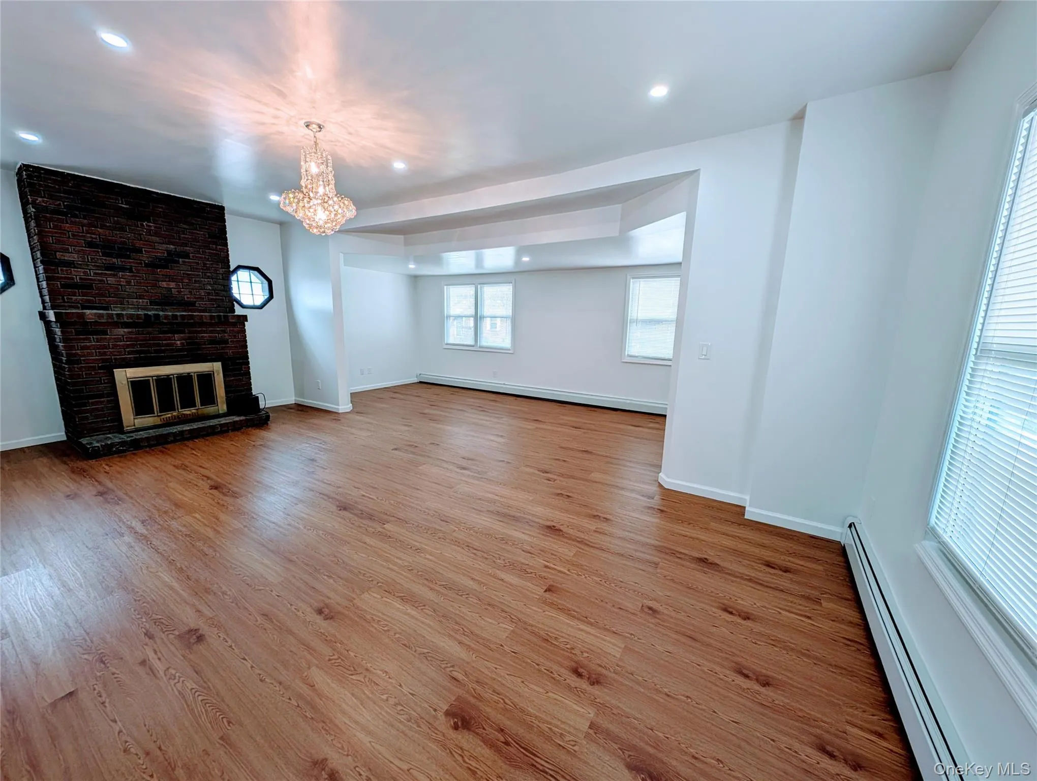 Unfurnished living room featuring a baseboard radiator, an inviting chandelier, baseboards, and light wood-type flooring Unfurnished living room featuring a baseboard radiator, an inviting chandelier, baseboards, and light wood-type flooring