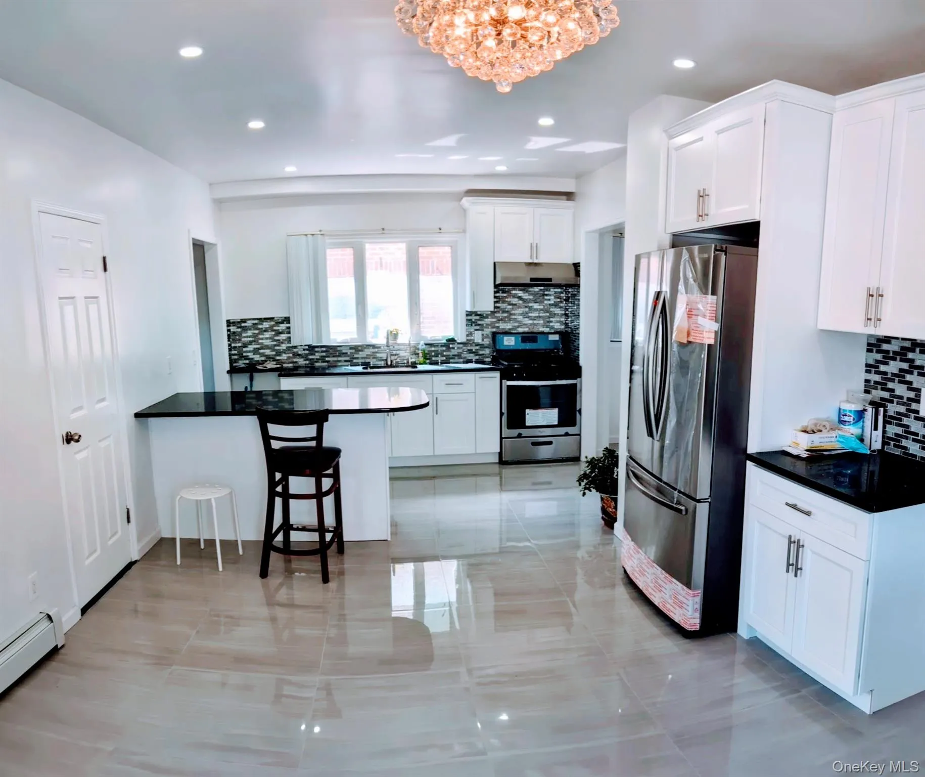 Kitchen with a peninsula, a chandelier, stainless steel appliances, a baseboard radiator, and decorative backsplash Kitchen with a peninsula, a chandelier, stainless steel appliances, a baseboard radiator, and decorative backsplash