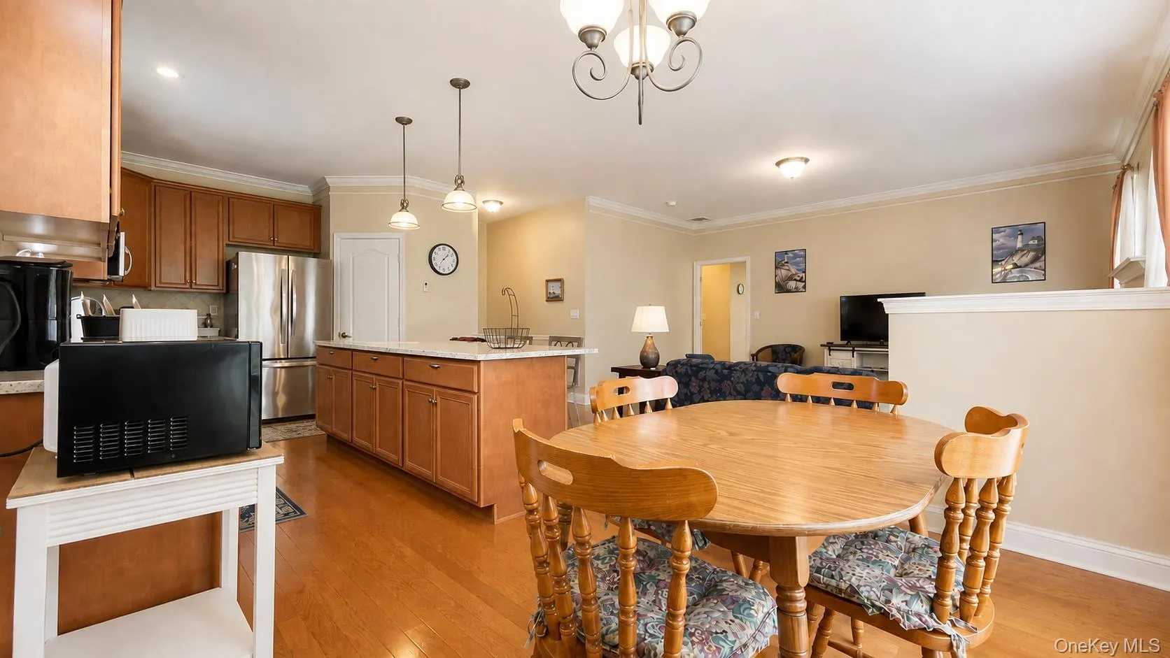 Open-concept kitchen featuring wood cabinetry, stainless steel refrigerator, and a kitchen island with pendant lighting Open-concept kitchen featuring wood cabinetry, stainless steel refrigerator, and a kitchen island with pendant lighting