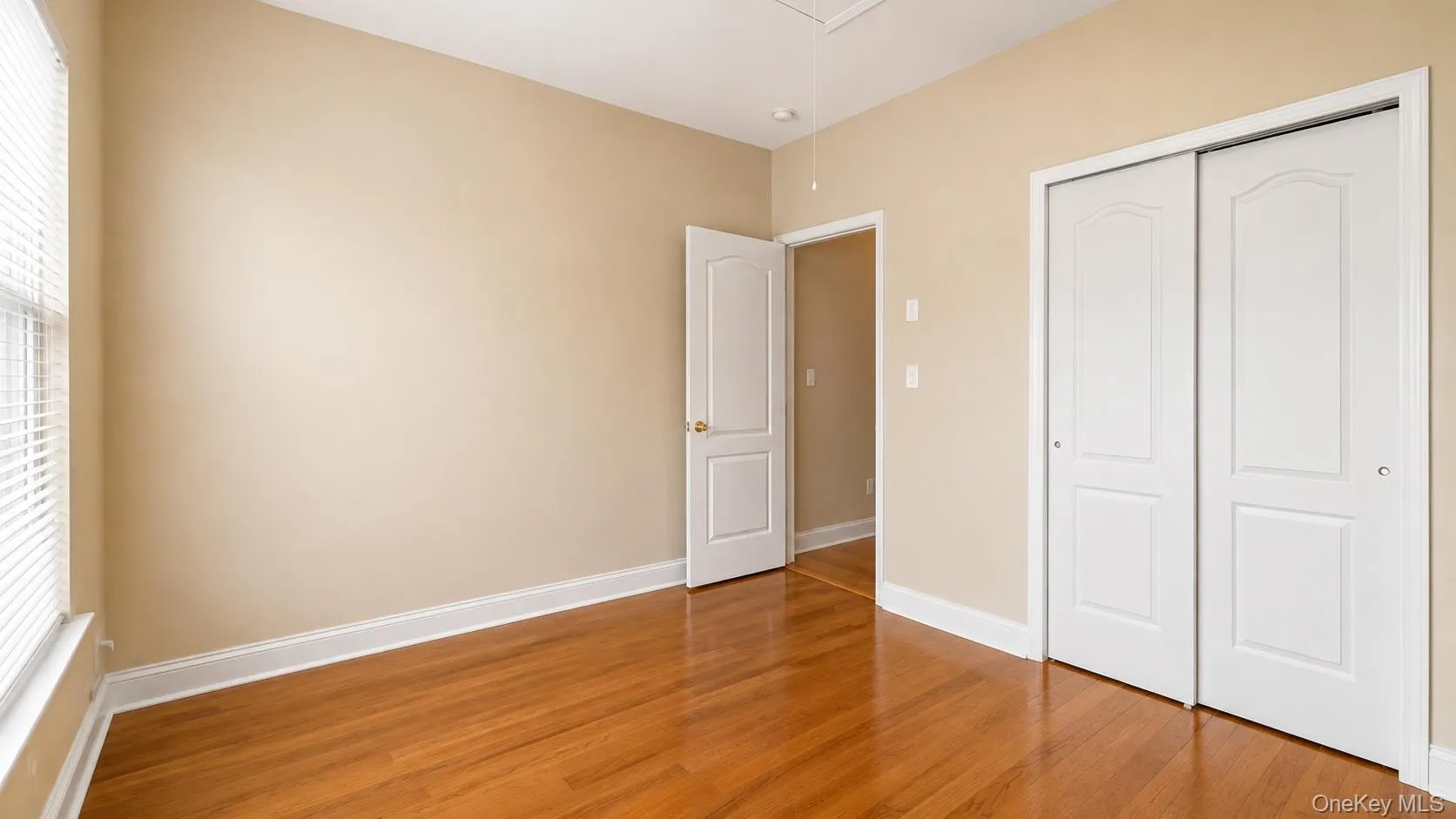 Hardwood flooring, painted walls, white trim, window with blinds, and bi-fold closet doors Hardwood flooring, painted walls, white trim, window with blinds, and bi-fold closet doors