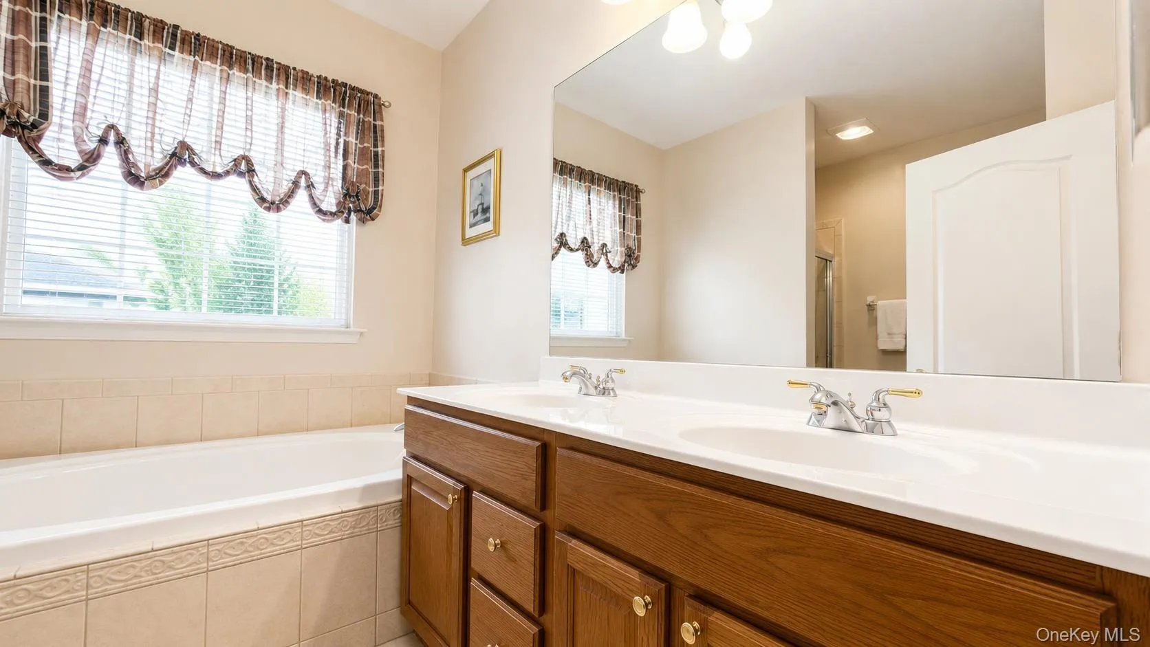 Dual vanity with integrated sinks, wood-finish cabinetry, built-in bathtub, and tiled surround Dual vanity with integrated sinks, wood-finish cabinetry, built-in bathtub, and tiled surround