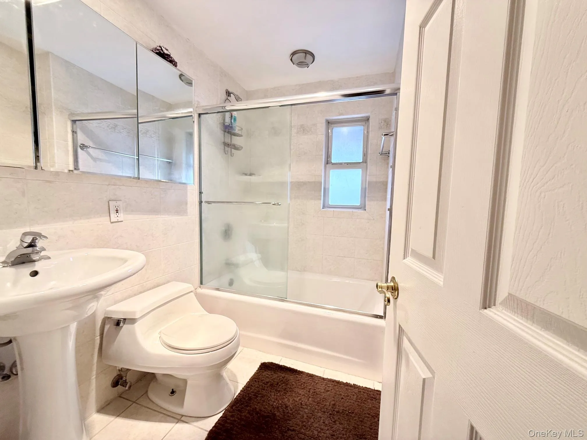 Bathroom featuring a pedestal sink, white toilet, and a bathtub with sliding glass doors Bathroom featuring a pedestal sink, white toilet, and a bathtub with sliding glass doors
