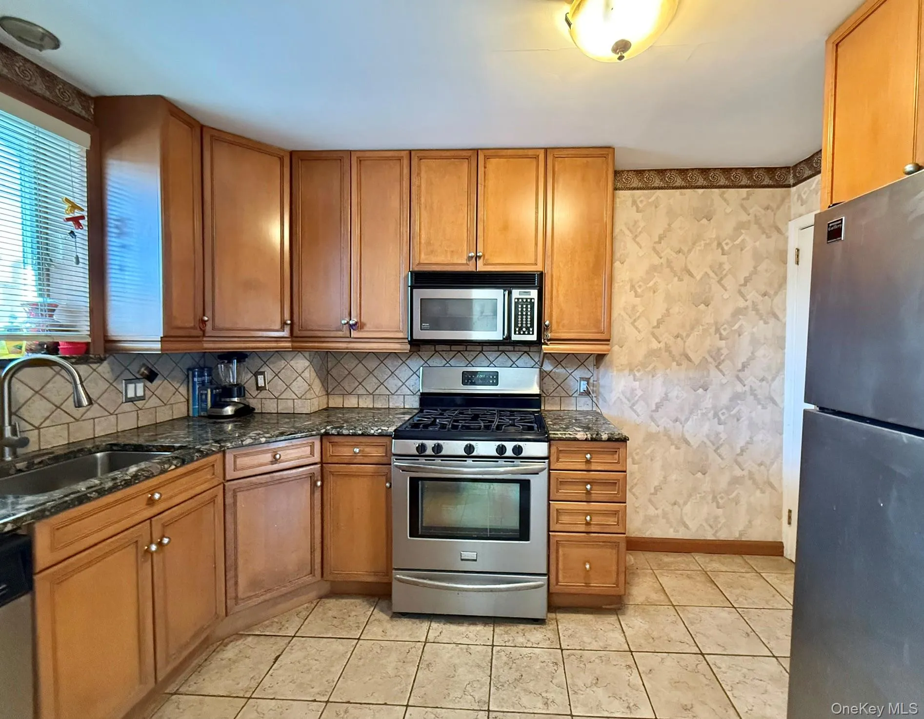 Kitchen featuring wood cabinetry, stainless steel appliances, dark stone countertops, and a diagonal tile backsplash Kitchen featuring wood cabinetry, stainless steel appliances, dark stone countertops, and a diagonal tile backsplash