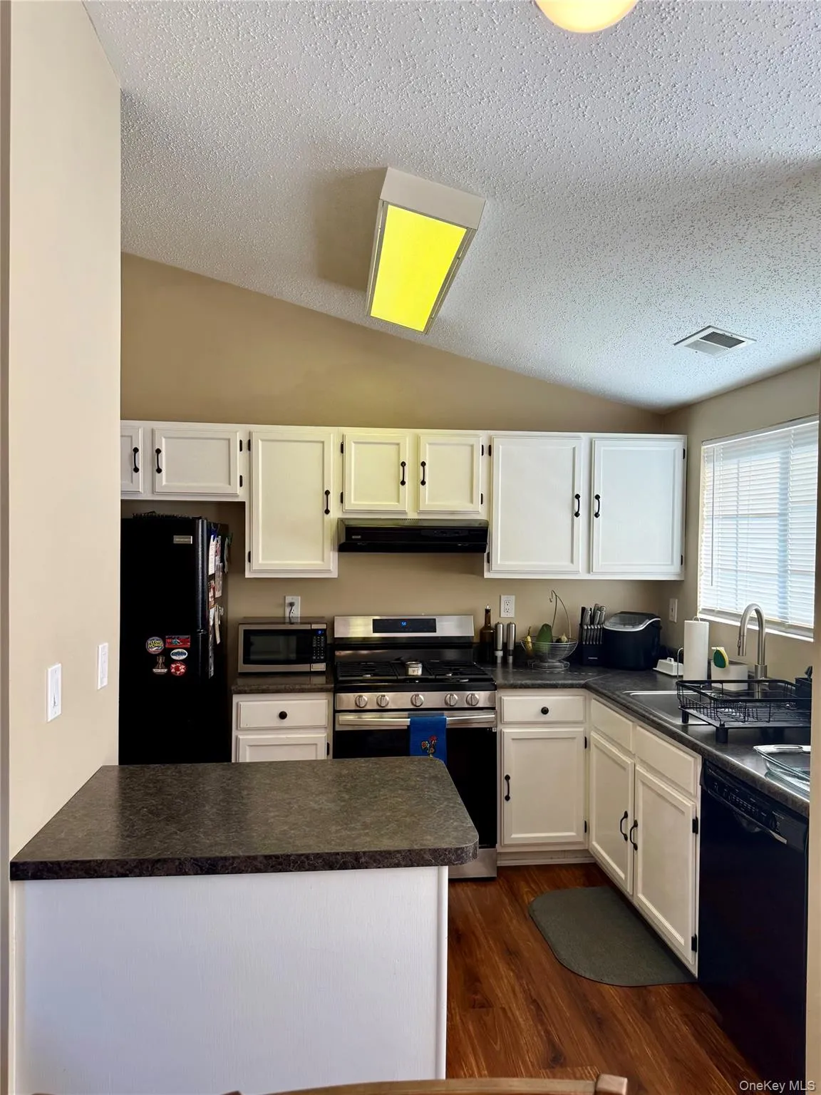 Kitchen featuring lofted ceiling, dark countertops, black appliances, white cabinets, and dark wood finished floors Kitchen featuring lofted ceiling, dark countertops, black appliances, white cabinets, and dark wood finished floors