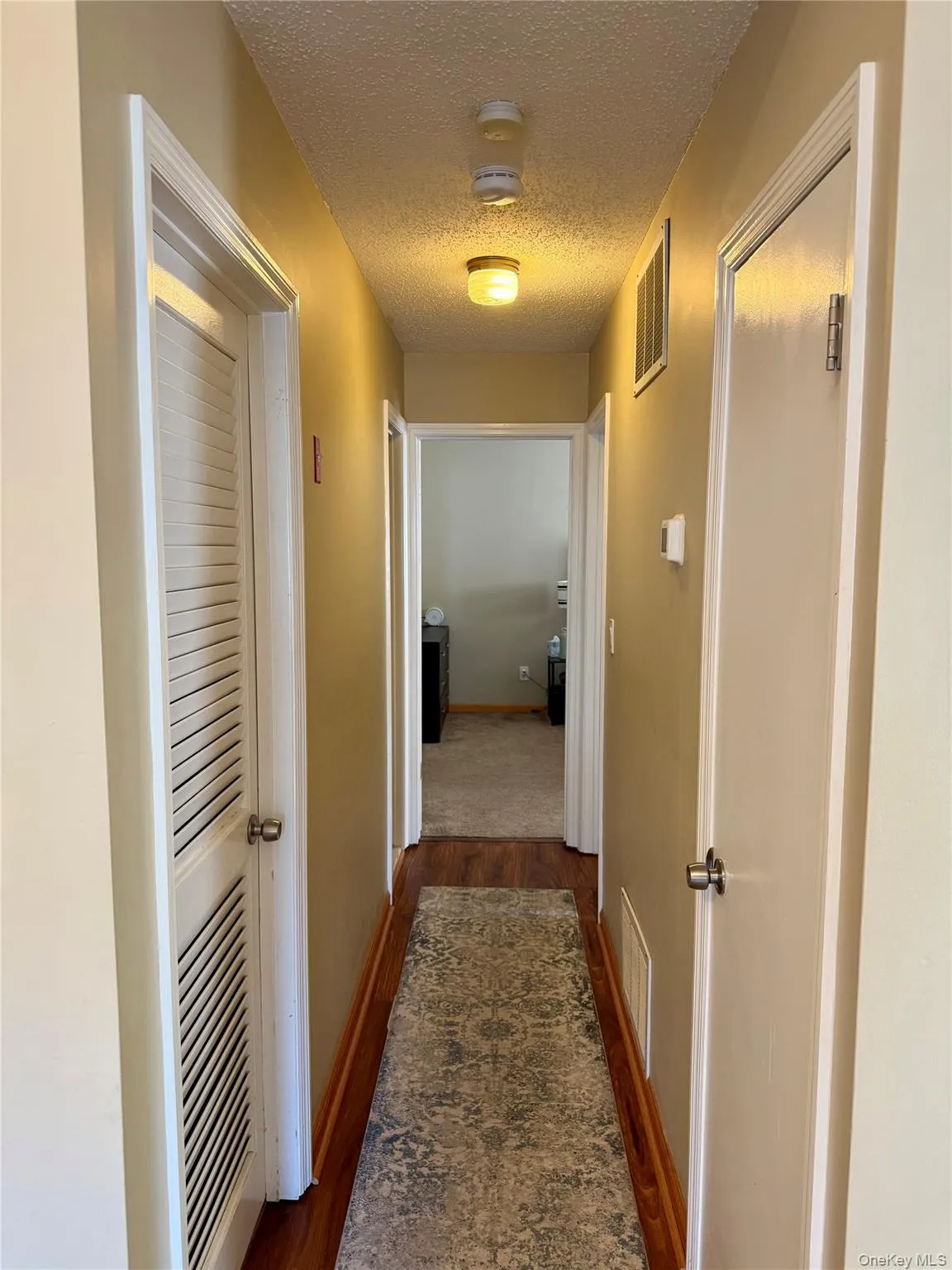 Hallway with a textured ceiling and dark wood-type flooring Hallway with a textured ceiling and dark wood-type flooring