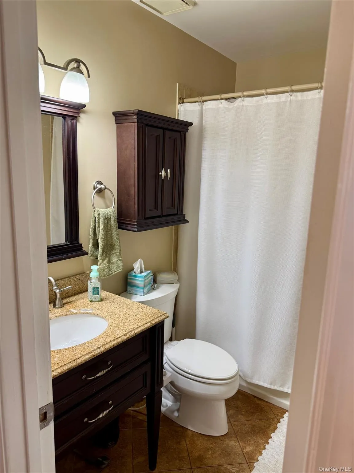 Bathroom with dark tile patterned floors, vanity, and curtained shower Bathroom with dark tile patterned floors, vanity, and curtained shower