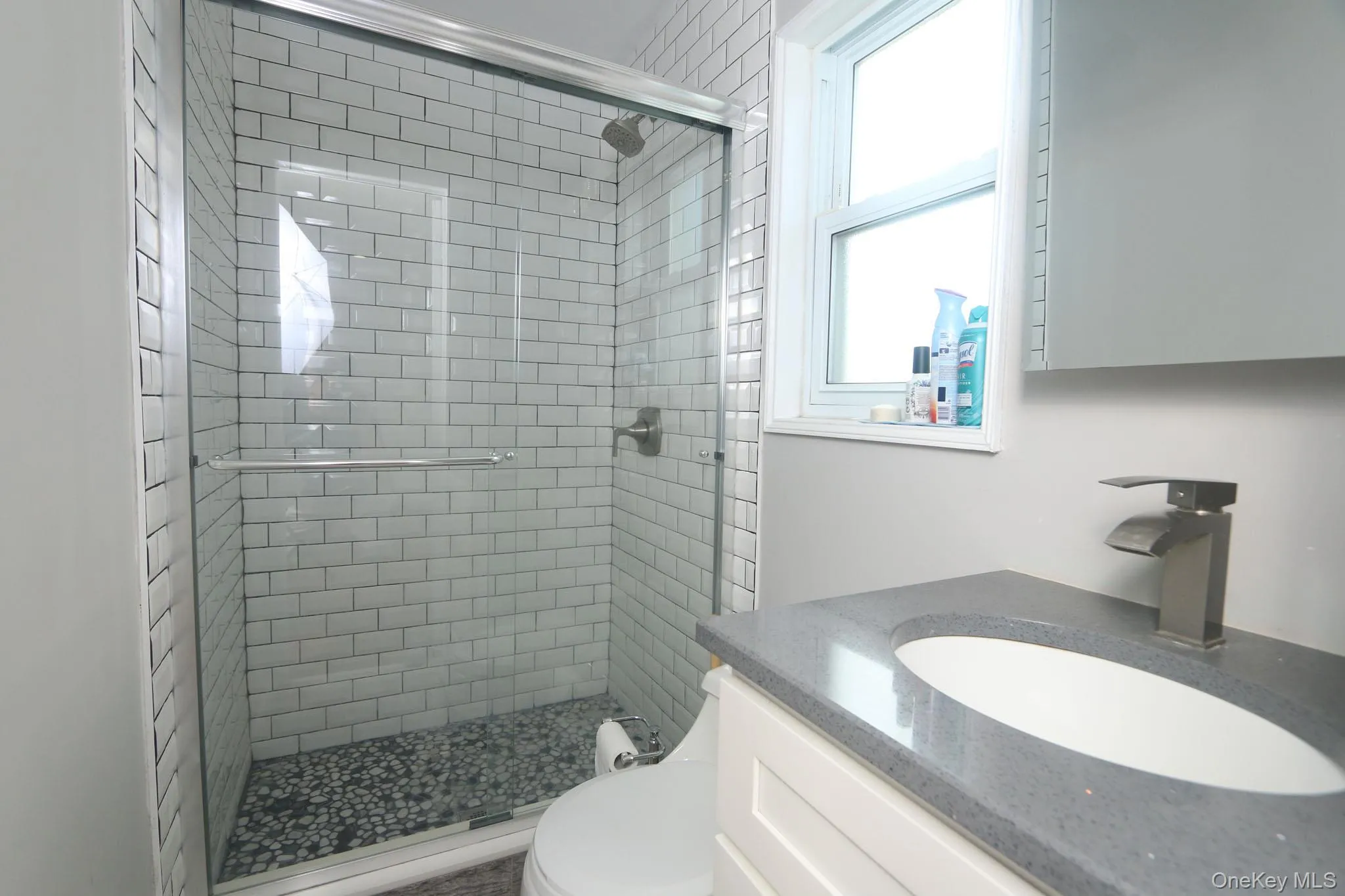 Bathroom featuring a subway tile shower with pebble flooring and clear glass enclosure Bathroom featuring a subway tile shower with pebble flooring and clear glass enclosure