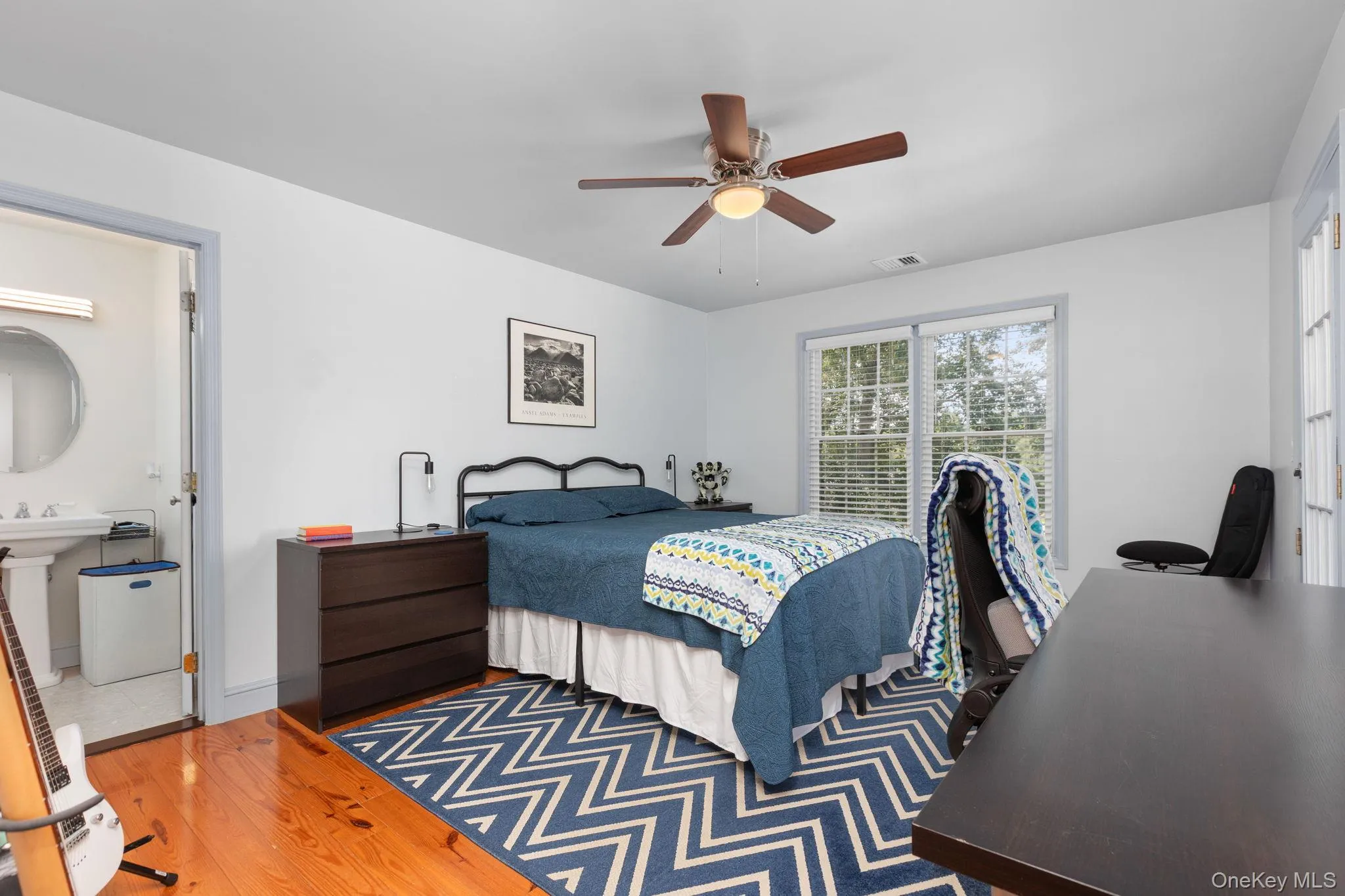 Hardwood flooring throughout this room, featuring a ceiling fan, glass door leading to balcony, and a full bathroom with a pedestal sink. Hardwood flooring throughout this room, featuring a ceiling fan, glass door leading to balcony, and a full bathroom with a pedestal sink.