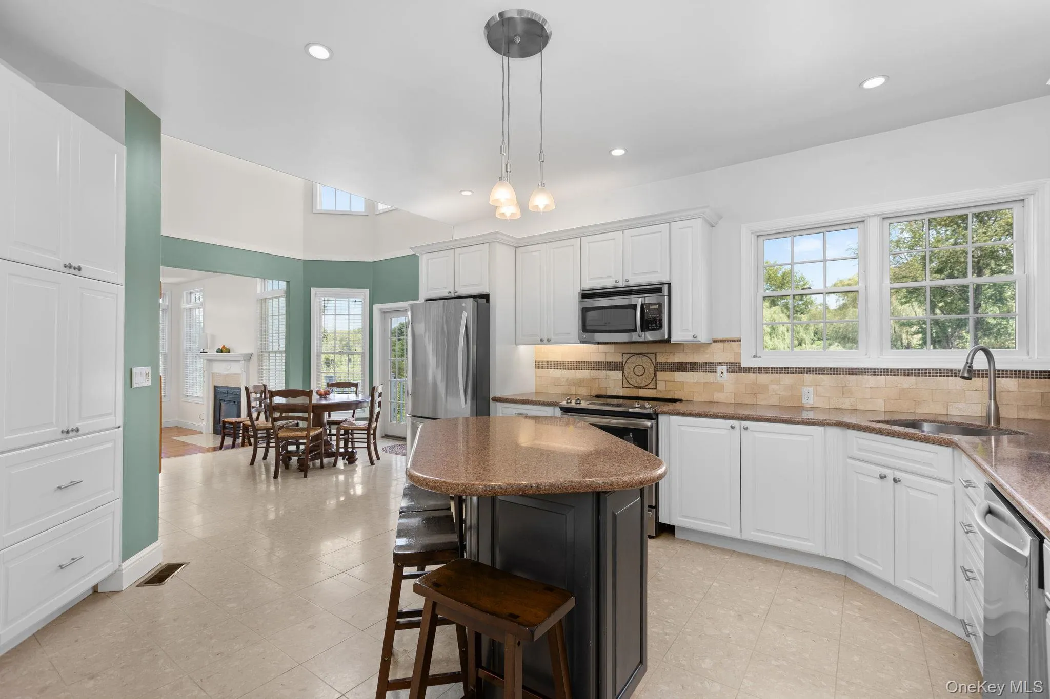 Spacious kitchen featuring an island with seating, stainless steel appliances, white cabinetry, cream tile flooring, and a tiled backsplash Spacious kitchen featuring an island with seating, stainless steel appliances, white cabinetry, cream tile flooring, and a tiled backsplash