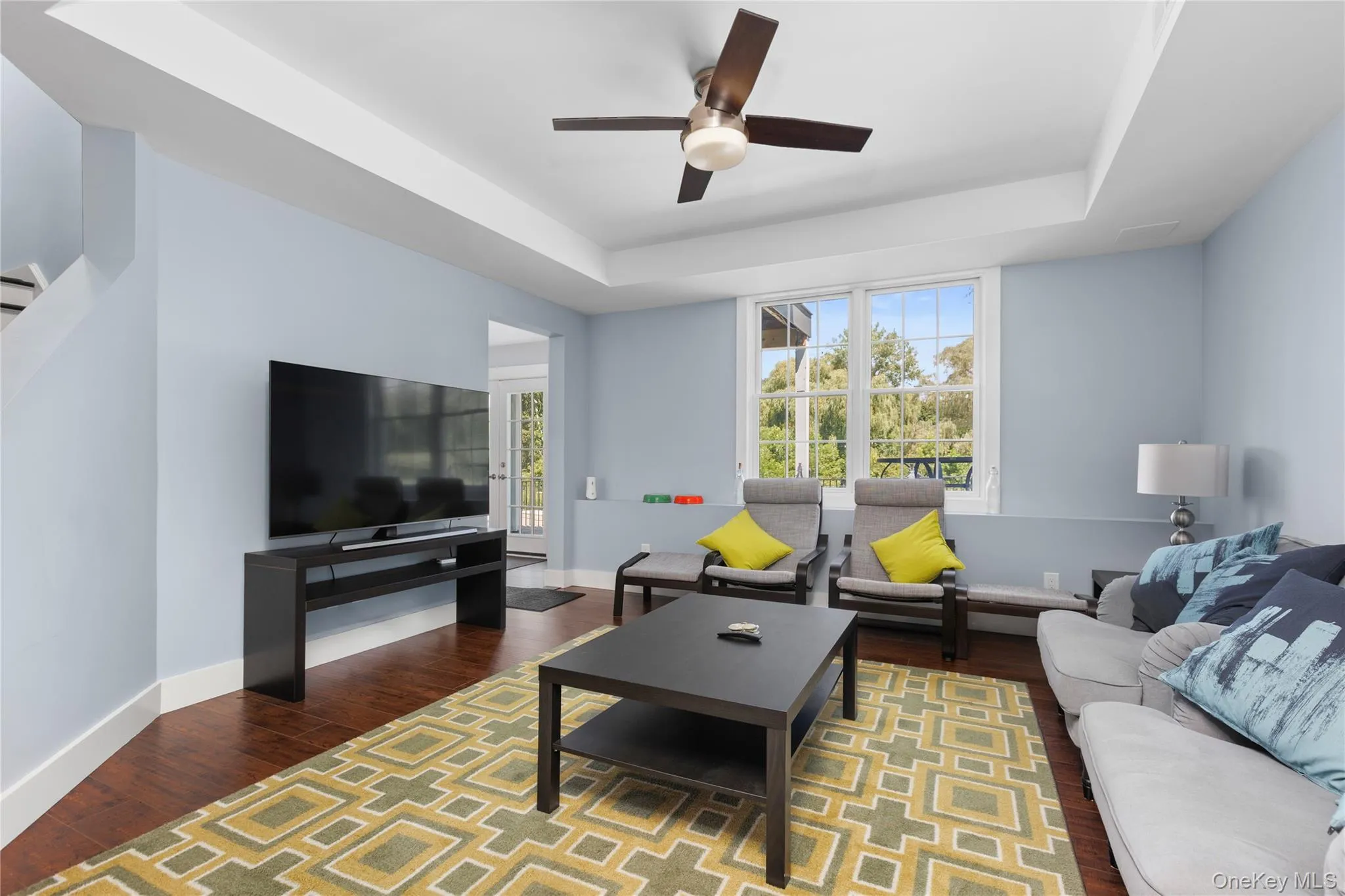 Spacious living area featuring hard wood flooring, a tray ceiling with a built-in ceiling fan, and light blue walls. Spacious living area featuring hard wood flooring, a tray ceiling with a built-in ceiling fan, and light blue walls.