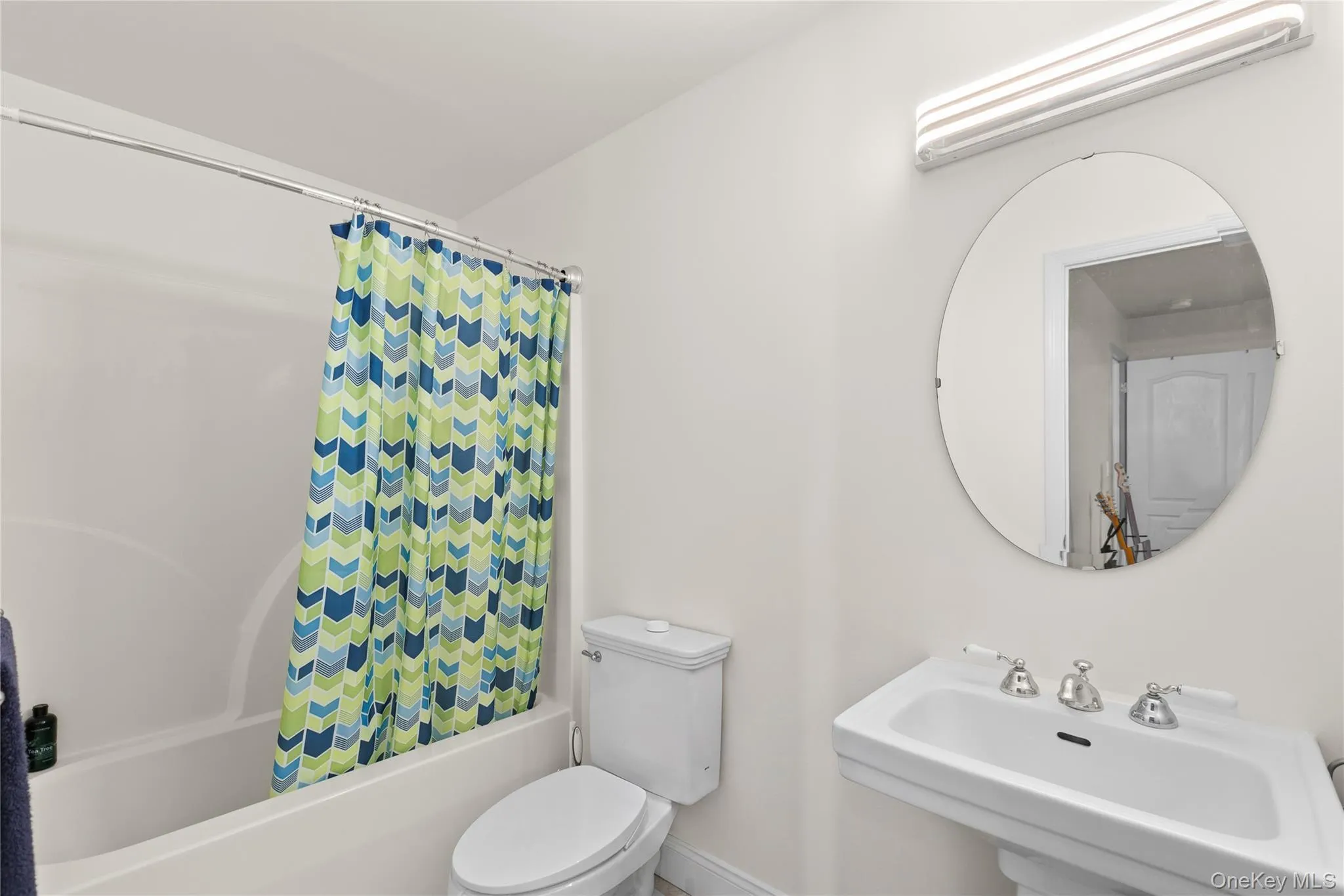 Tub and shower combination, pedestal sink with chrome fixtures, oval wall mirror, and overhead lighting Tub and shower combination, pedestal sink with chrome fixtures, oval wall mirror, and overhead lighting
