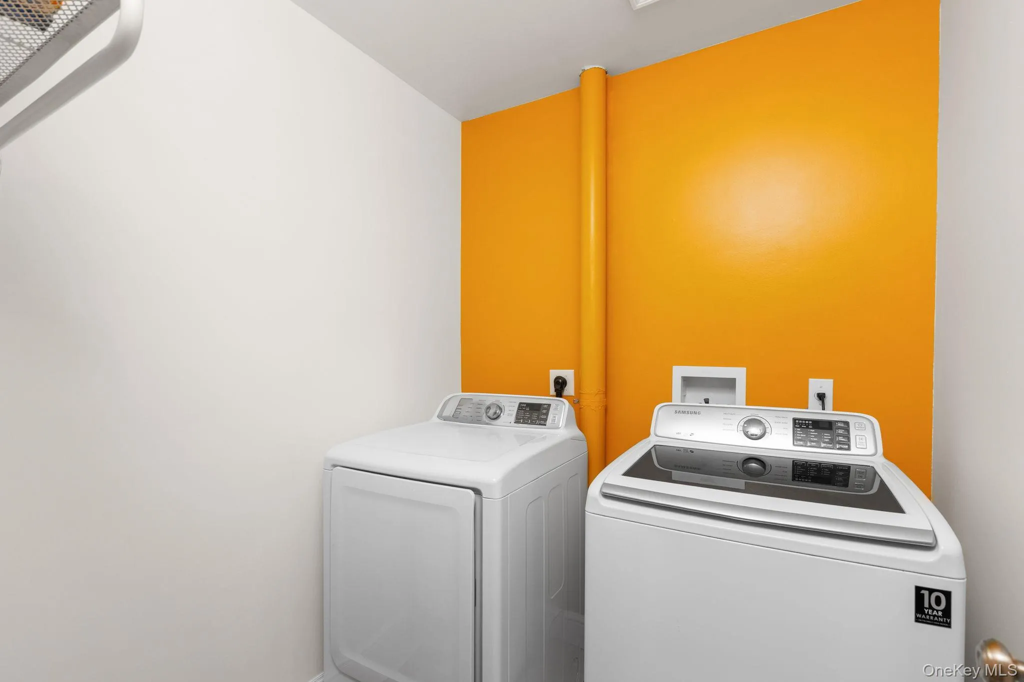 Dedicated laundry area featuring white walls and a contrasting orange accent wall. Dedicated laundry area featuring white walls and a contrasting orange accent wall.