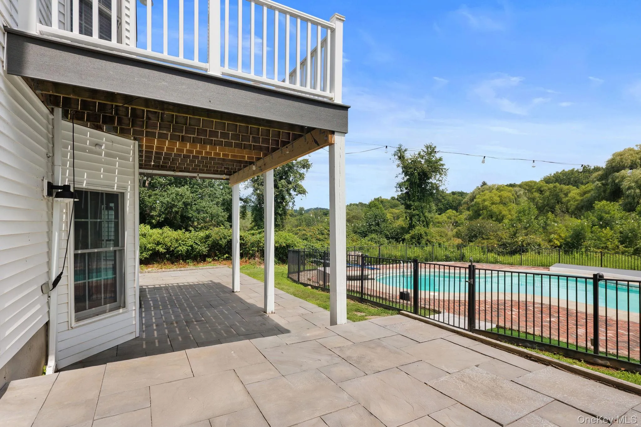 Outdoor patio with large format pavers, adjacent to a fenced in swimming pool with brick decking. Outdoor patio with large format pavers, adjacent to a fenced in swimming pool with brick decking.