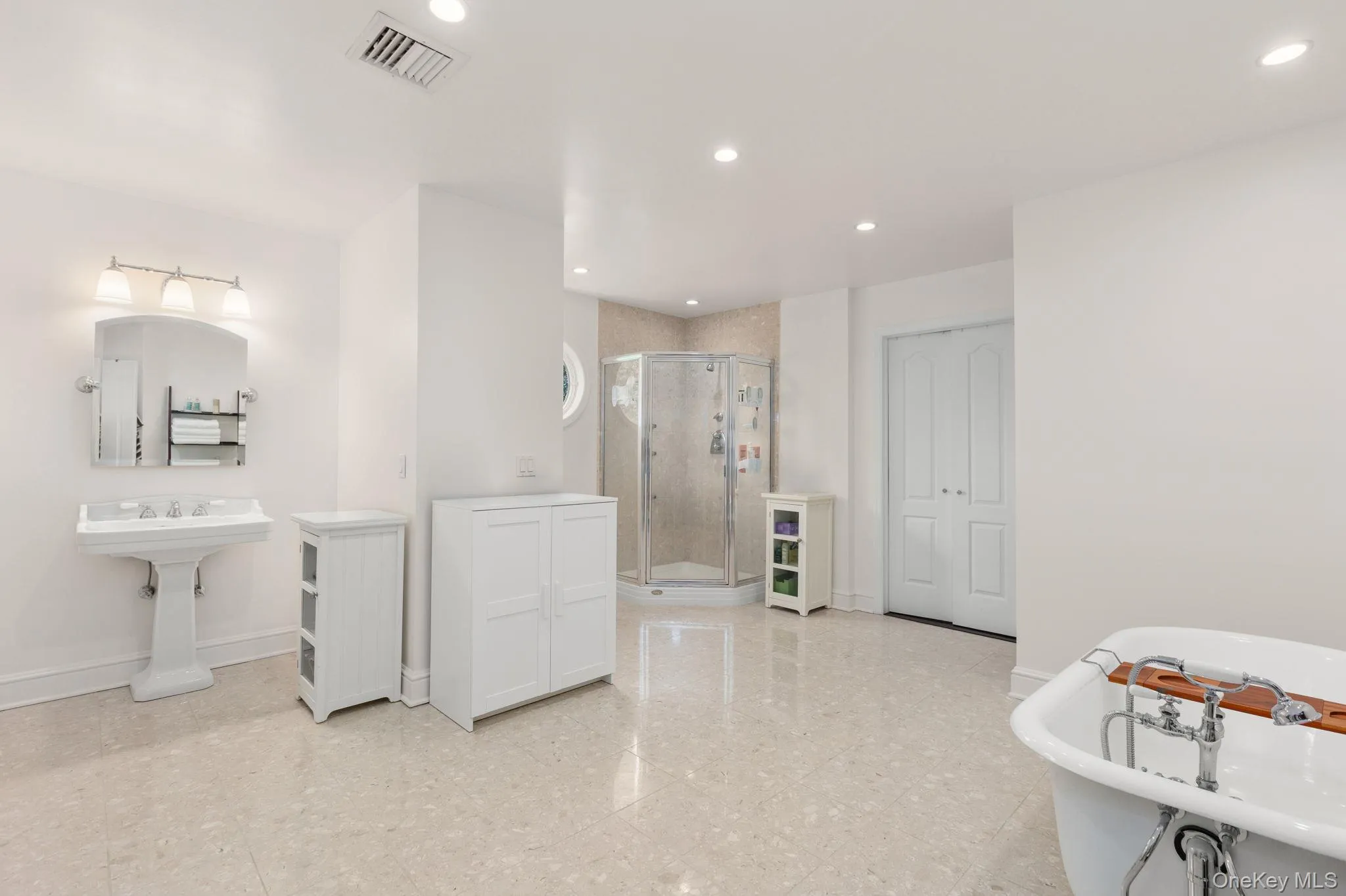 Spacious bathroom featuring a freestanding clawfoot tub, recessed lighting, double French doors, and cream tile flooring Spacious bathroom featuring a freestanding clawfoot tub, recessed lighting, double French doors, and cream tile flooring