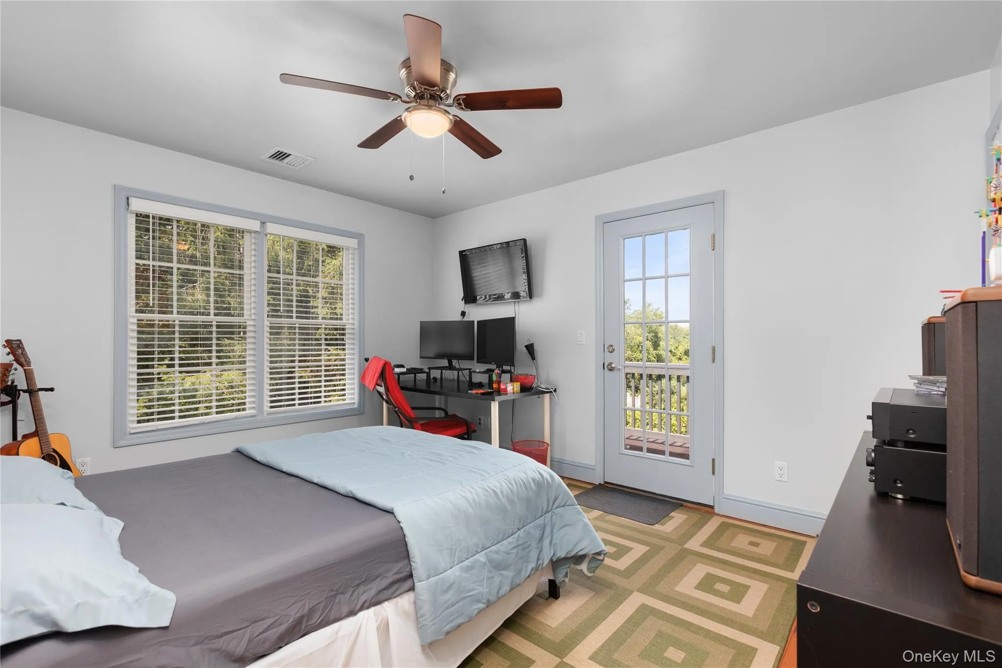 Bedroom featuring a ceiling fan with integrated lighting, dual windows with blinds, and a glass-paneled door opening to the exterior balcony. Bedroom featuring a ceiling fan with integrated lighting, dual windows with blinds, and a glass-paneled door opening to the exterior balcony.