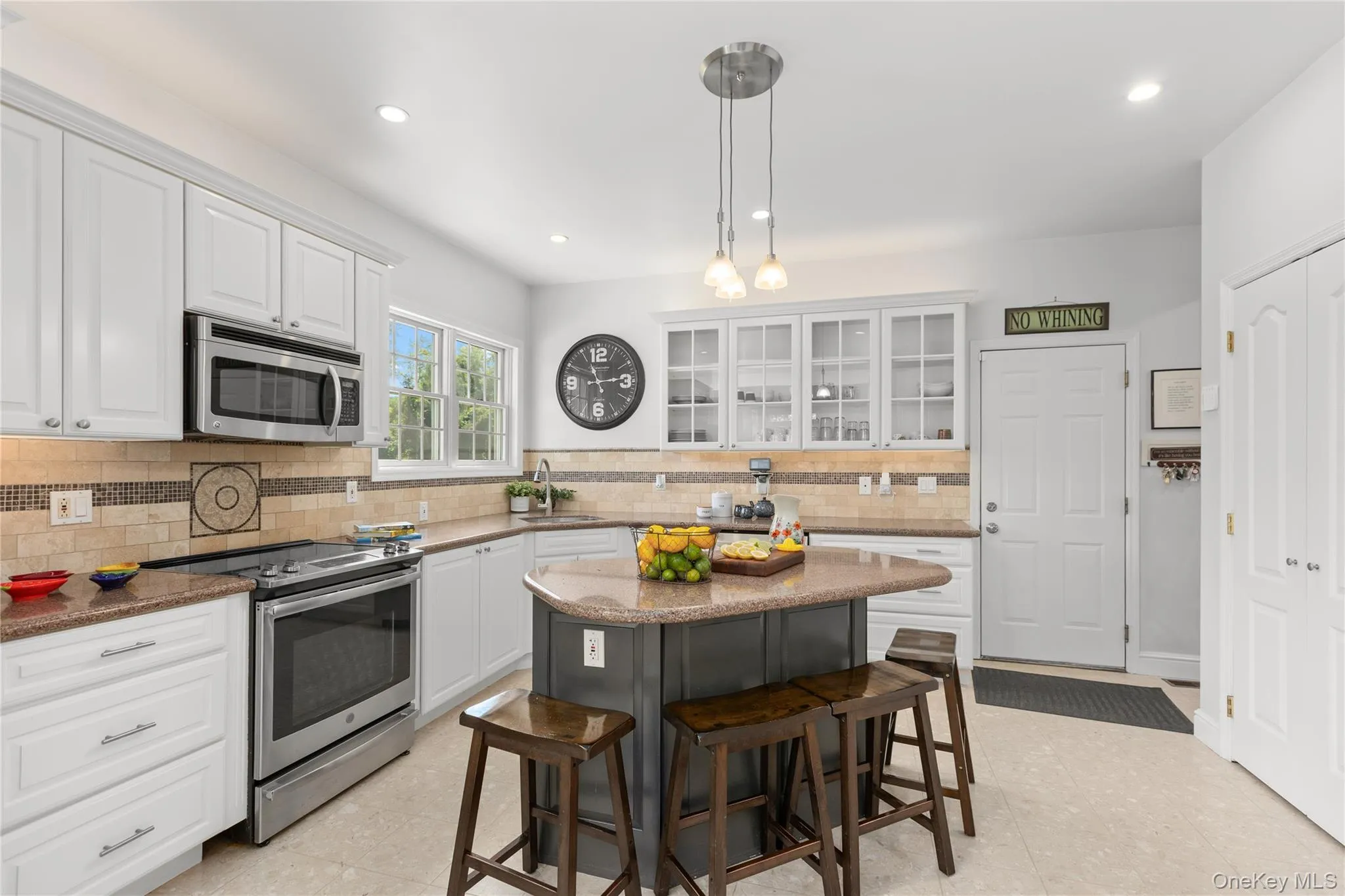 Spacious kitchen featuring an island with seating, stainless steel appliances, white cabinetry, cream tile flooring, and a tiled backsplas Spacious kitchen featuring an island with seating, stainless steel appliances, white cabinetry, cream tile flooring, and a tiled backsplas