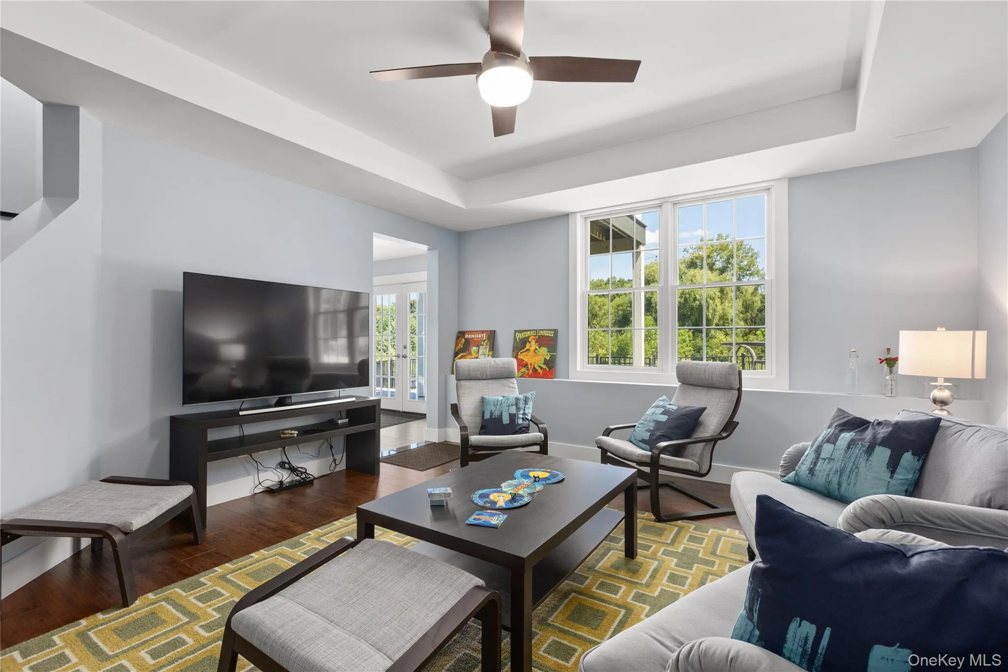 Living area featuring hard wood flooring, a tray ceiling with a ceiling fan, and large windows. Living area featuring hard wood flooring, a tray ceiling with a ceiling fan, and large windows.