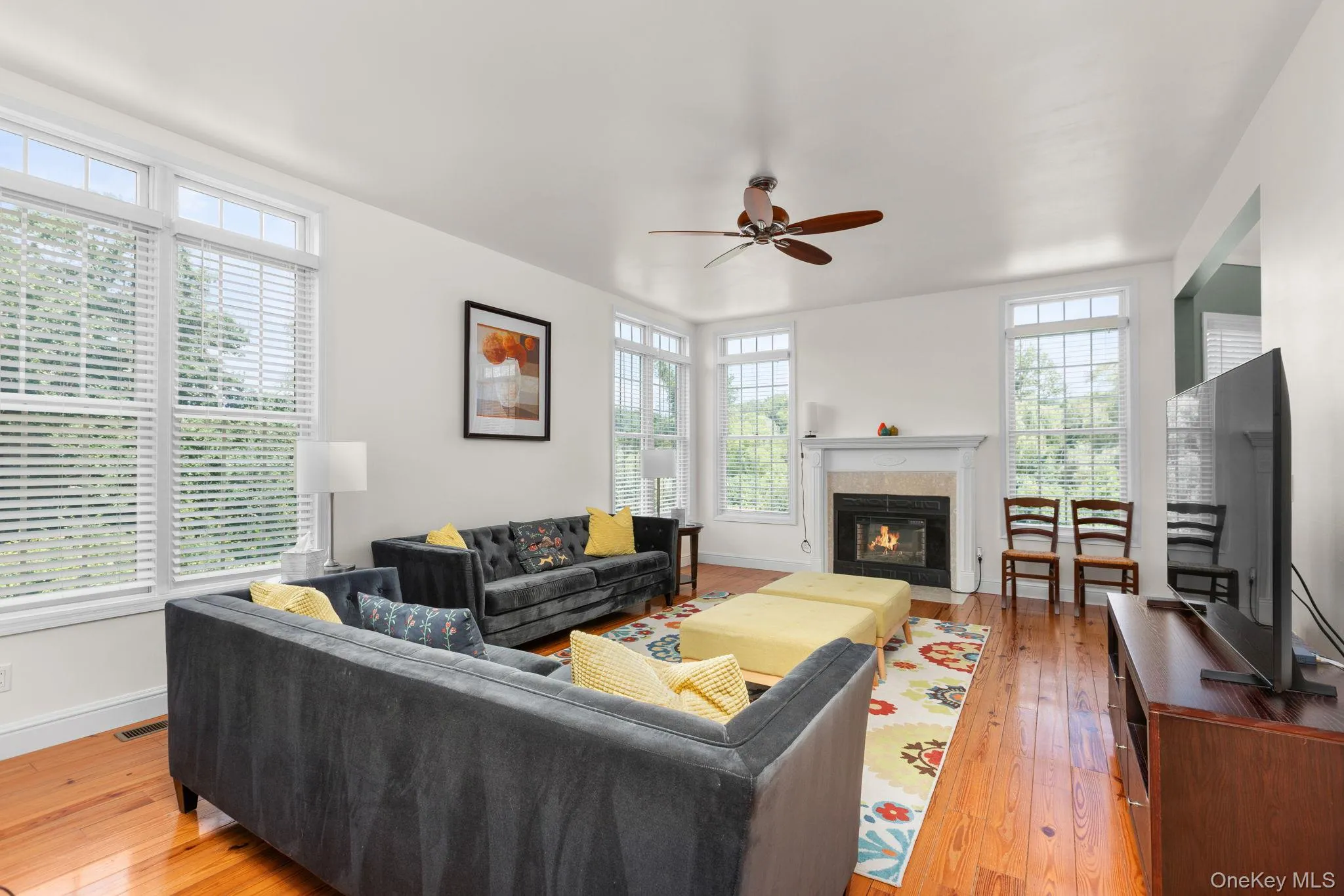 Hardwood flooring, multiple windows, built-in fireplace with mantel, ceiling fan, and white walls Hardwood flooring, multiple windows, built-in fireplace with mantel, ceiling fan, and white walls