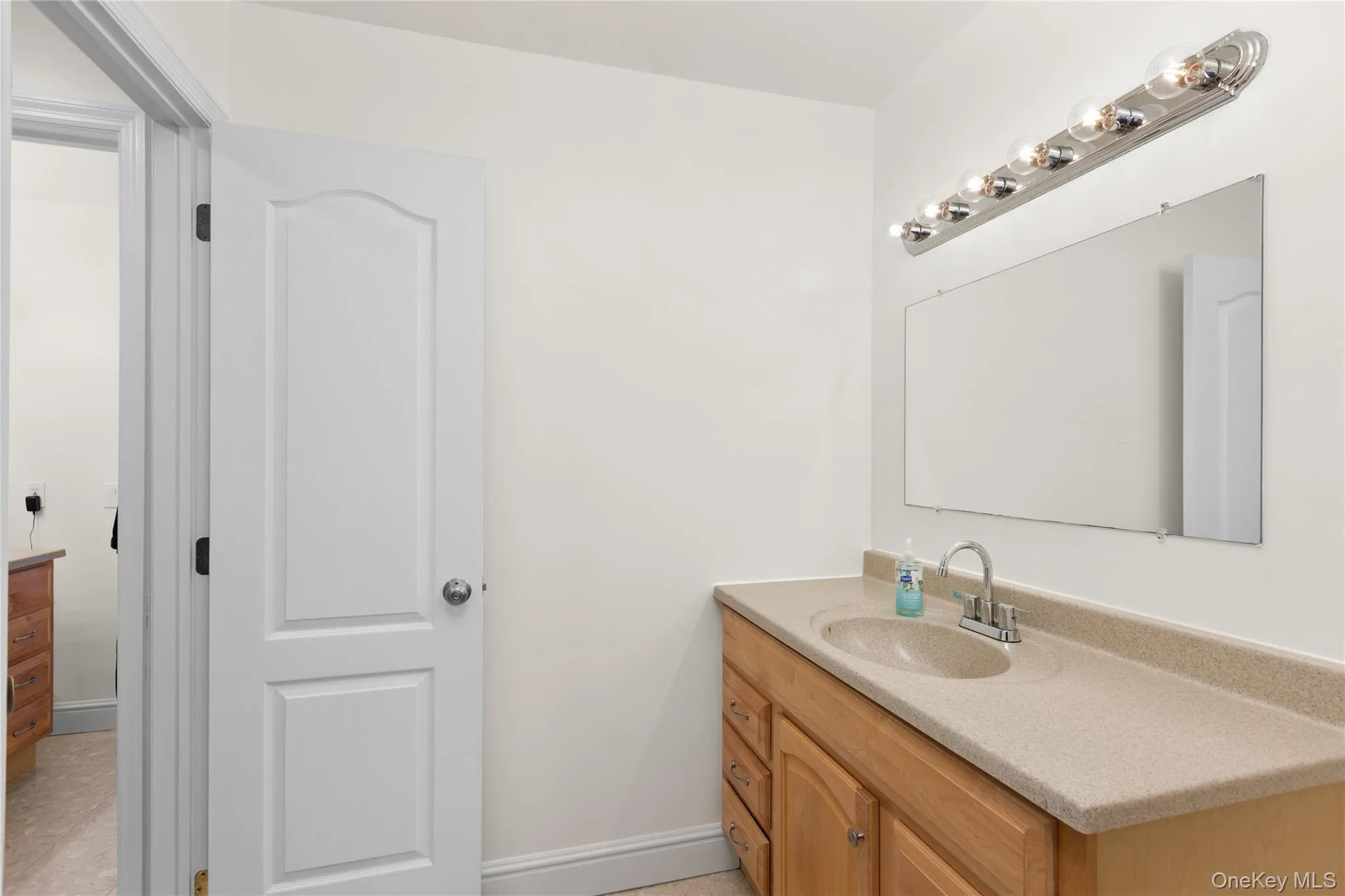 Bright bathroom featuring a wood-finish vanity with single sink configuration, light-toned countertop, and chrome fixtures Bright bathroom featuring a wood-finish vanity with single sink configuration, light-toned countertop, and chrome fixtures